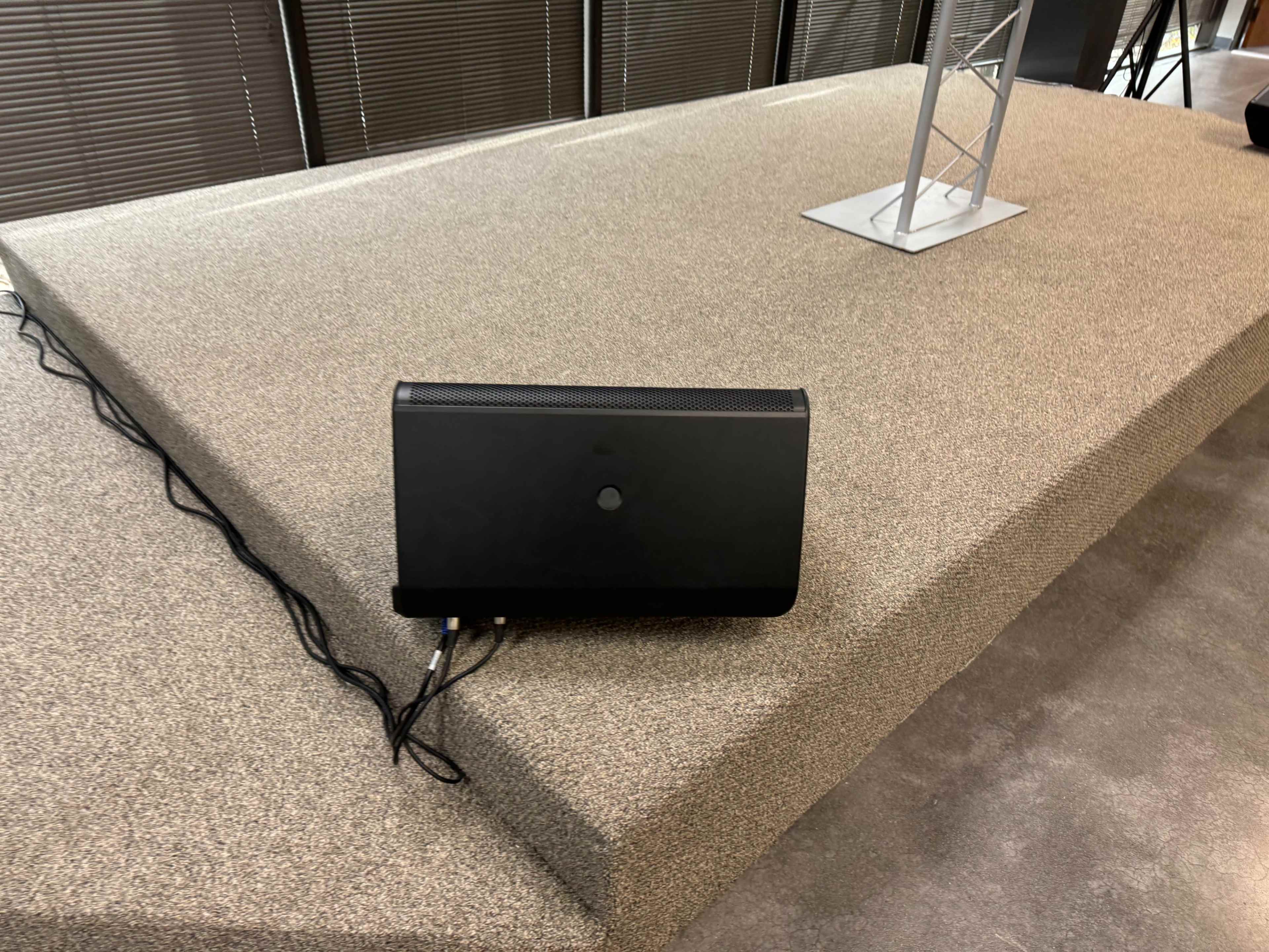 The image shows a black device placed on a raised, carpeted platform with visible cables connected to it.