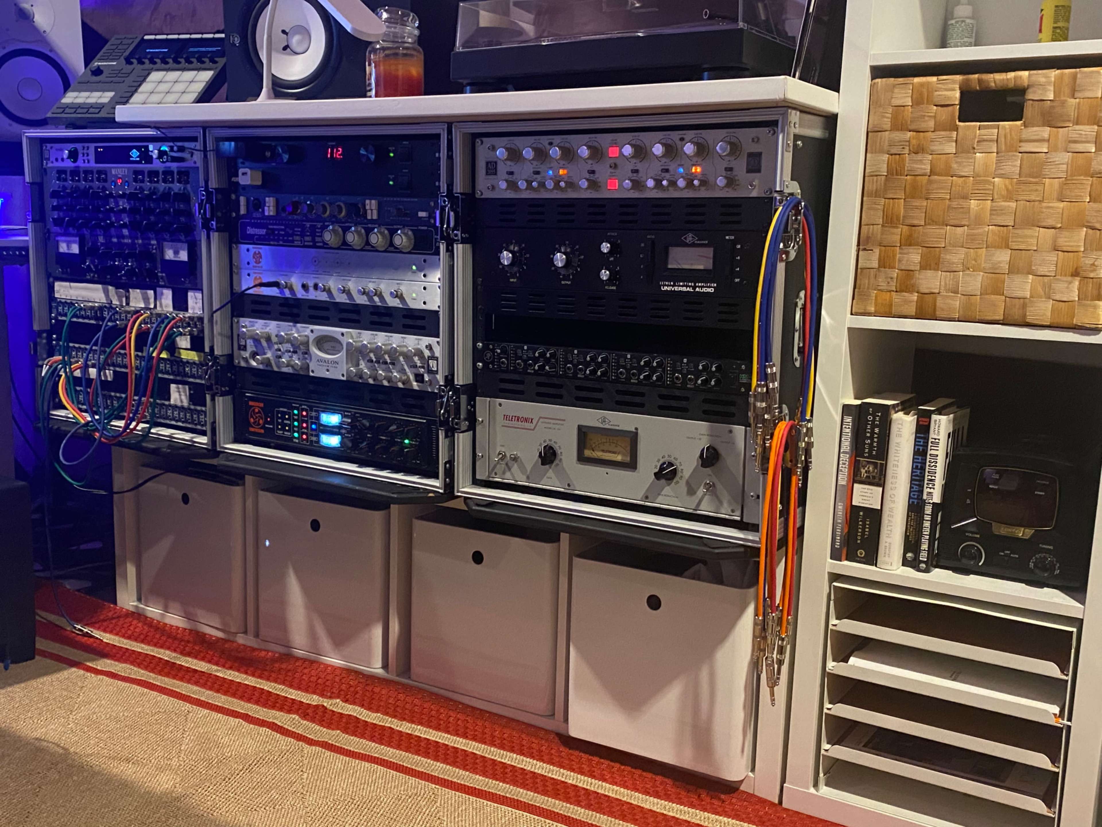 A music production setup with various audio equipment, including rack-mounted devices and organized cables, arranged on a shelving unit.