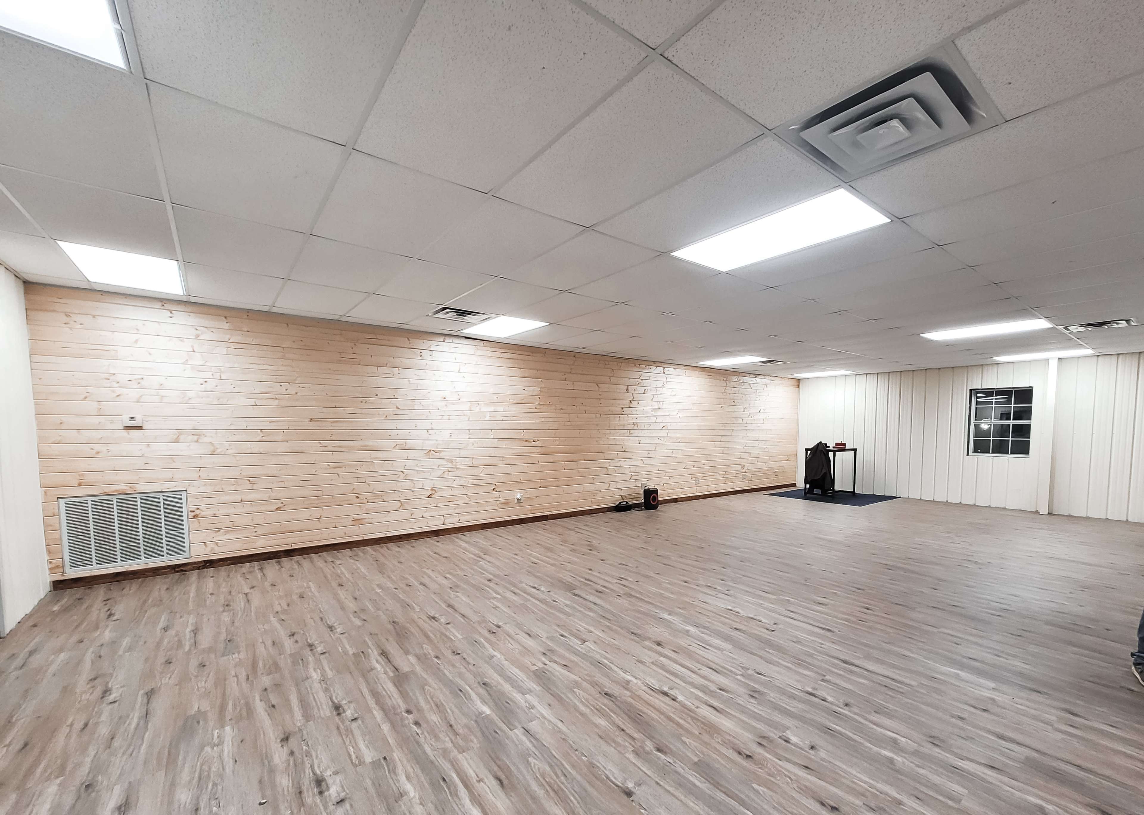 The image shows a spacious room with wooden paneling on one wall and a smooth, light-colored floor.