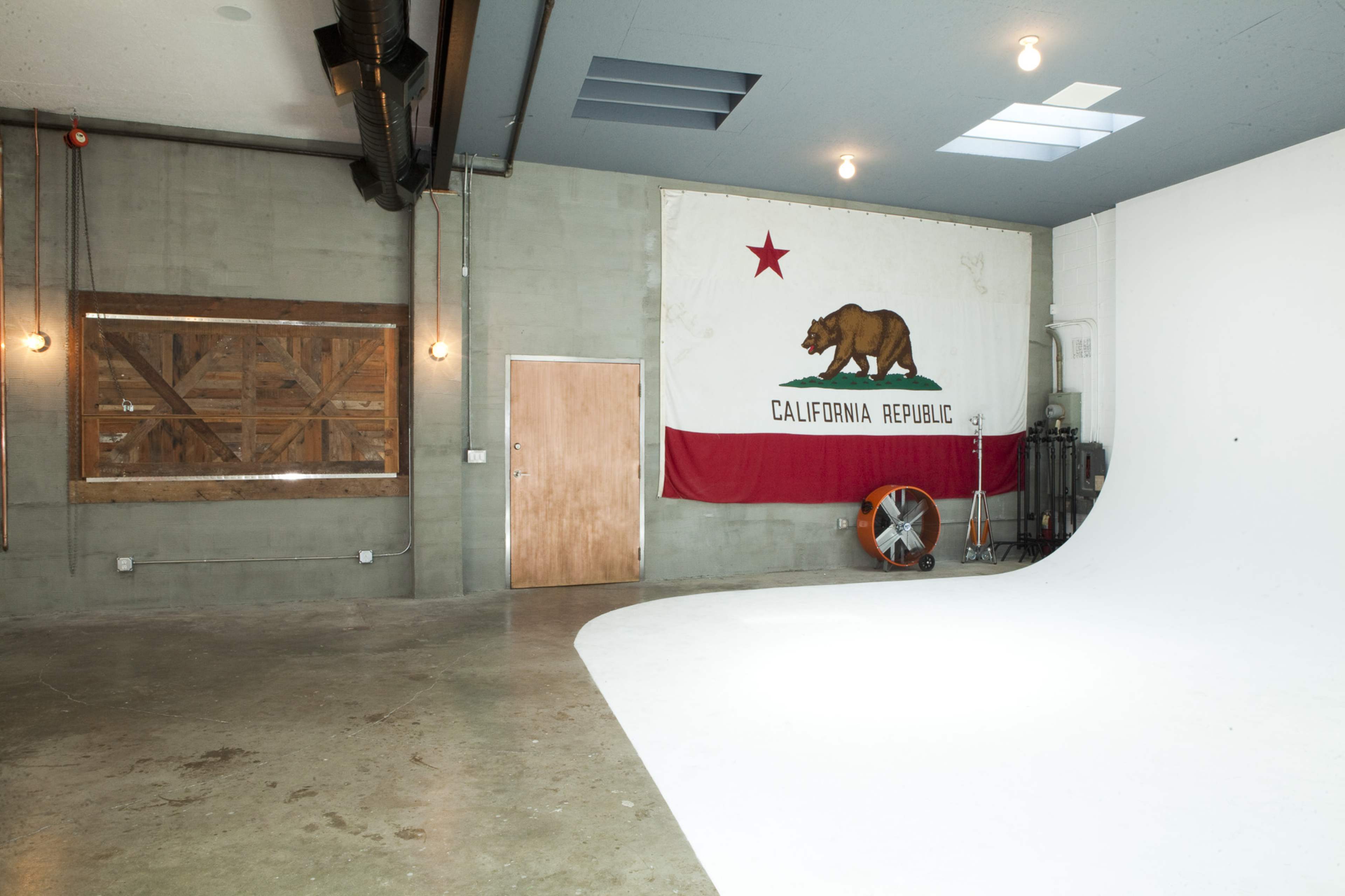 A spacious studio with a large California Republic flag mounted on the wall and a white curved backdrop in the foreground.