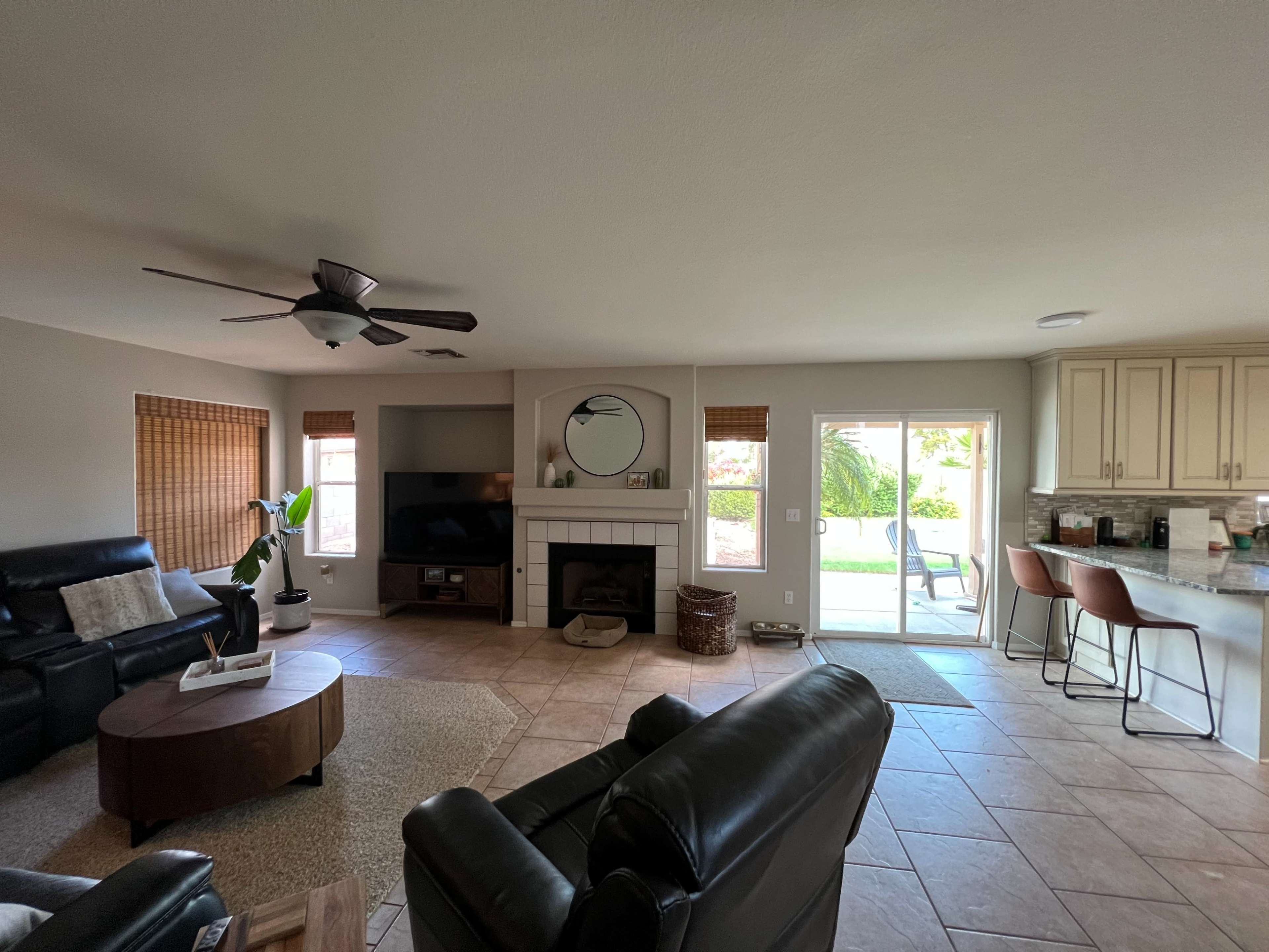 The living room features a seating area with black leather chairs, a round coffee table, a TV unit, and sliding glass doors leading to an outdoor space.
