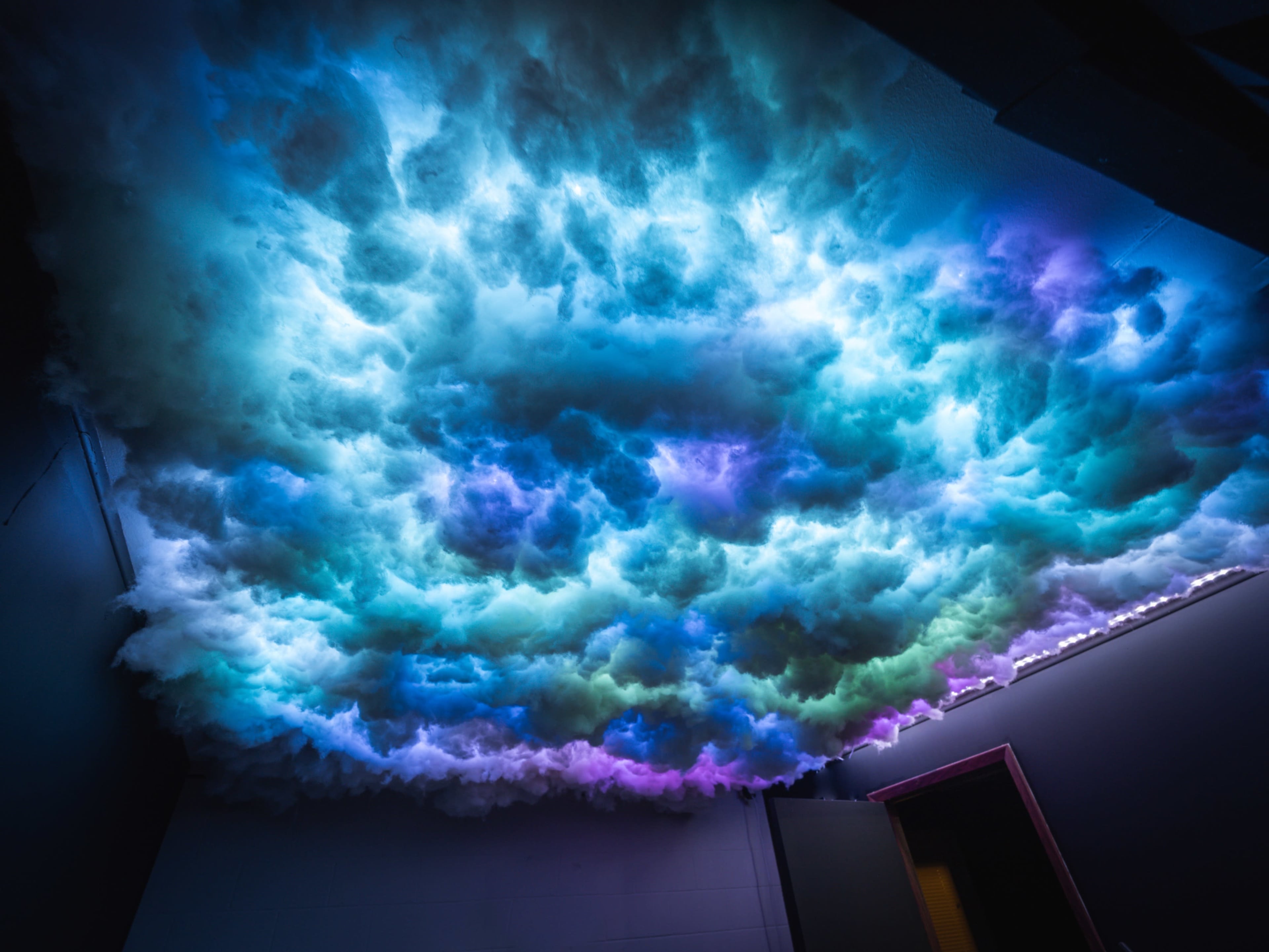 A colorful, illuminated cloud installation on a ceiling, blending shades of blue, purple, and white.