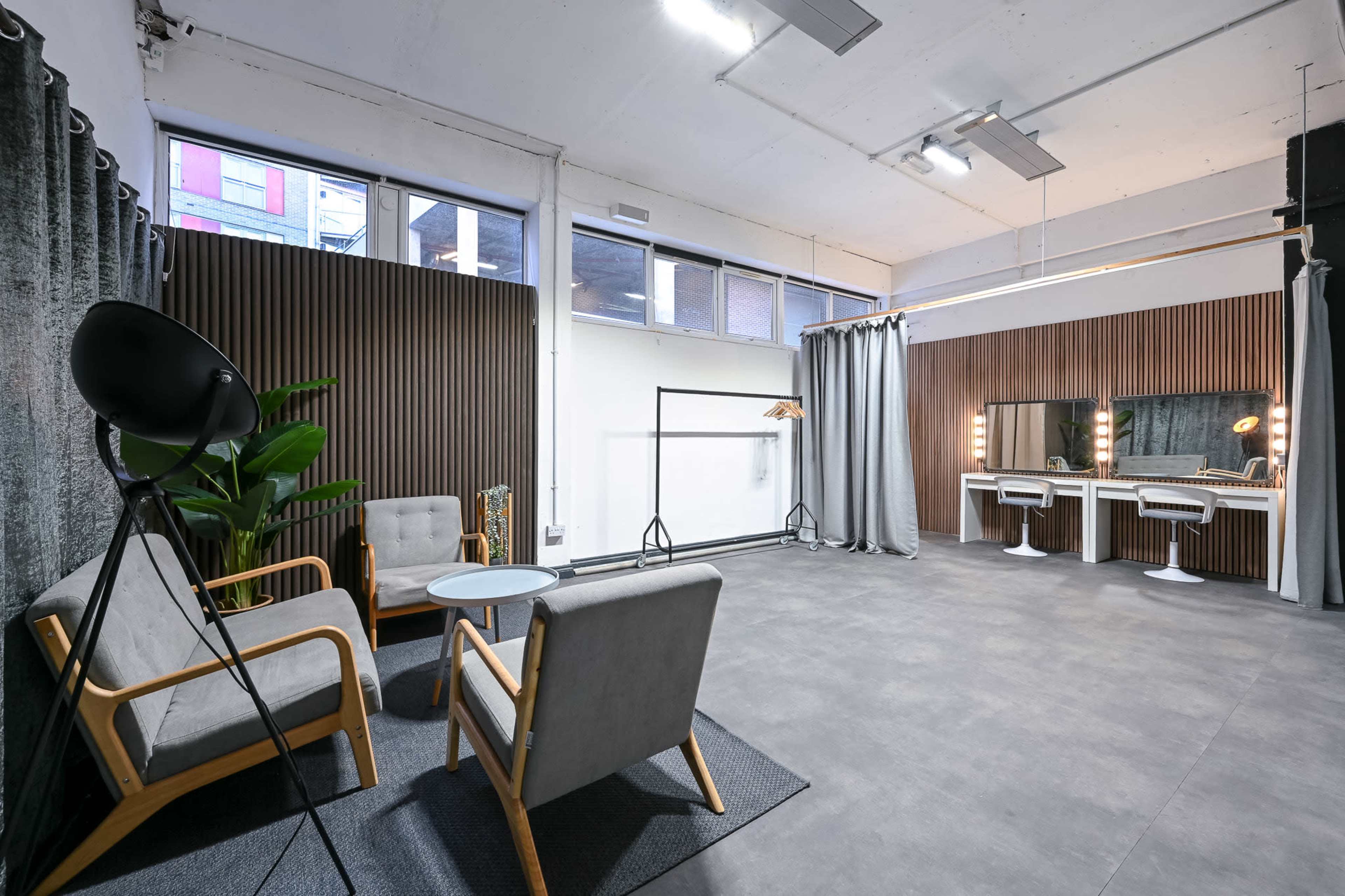 The image shows a modern, spacious interior with wooden paneling, two armchairs, a small table, and a vanity area with bright mirrors.