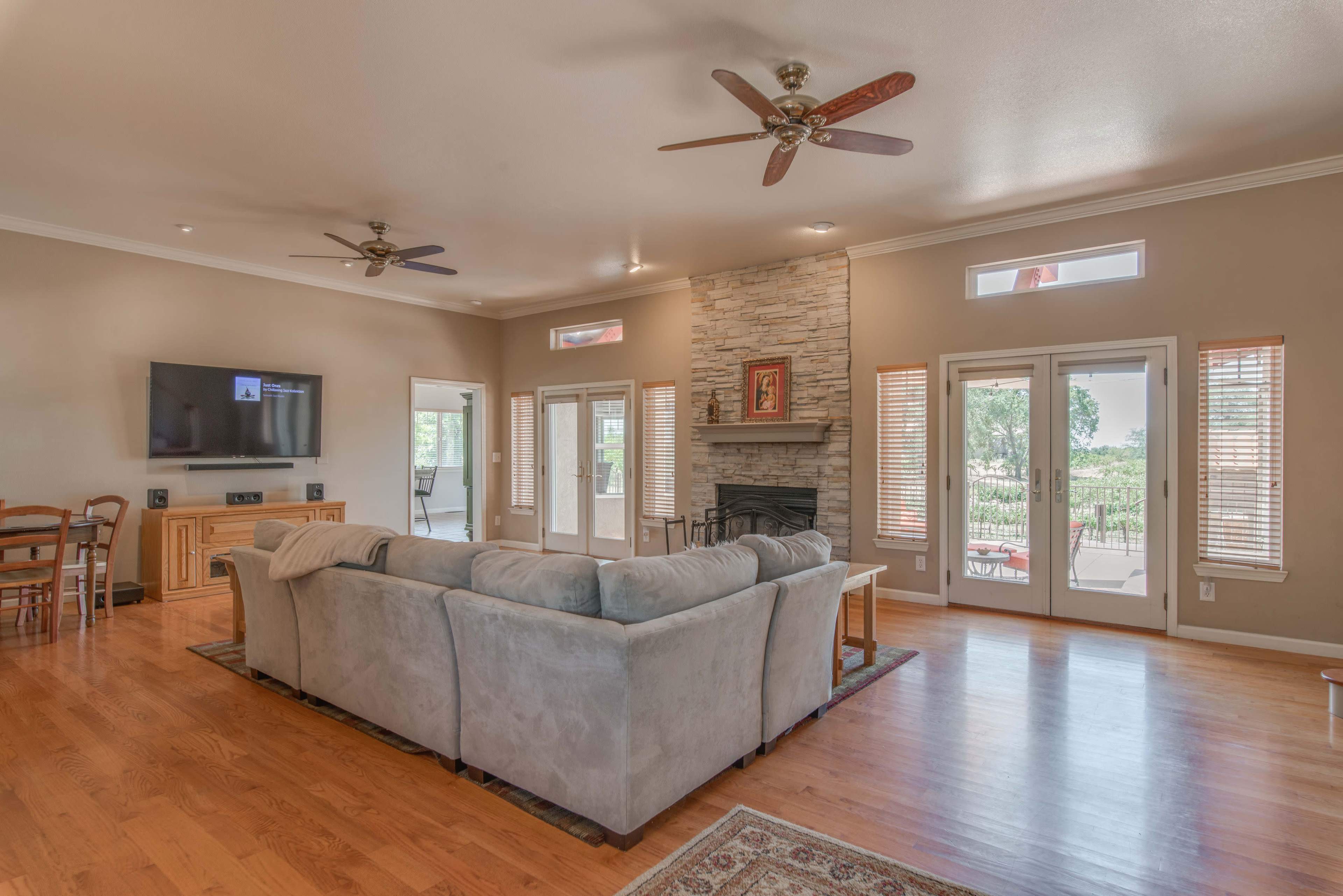 The image shows a spacious living room with a large sectional sofa, a stone fireplace, and multiple windows allowing natural light.