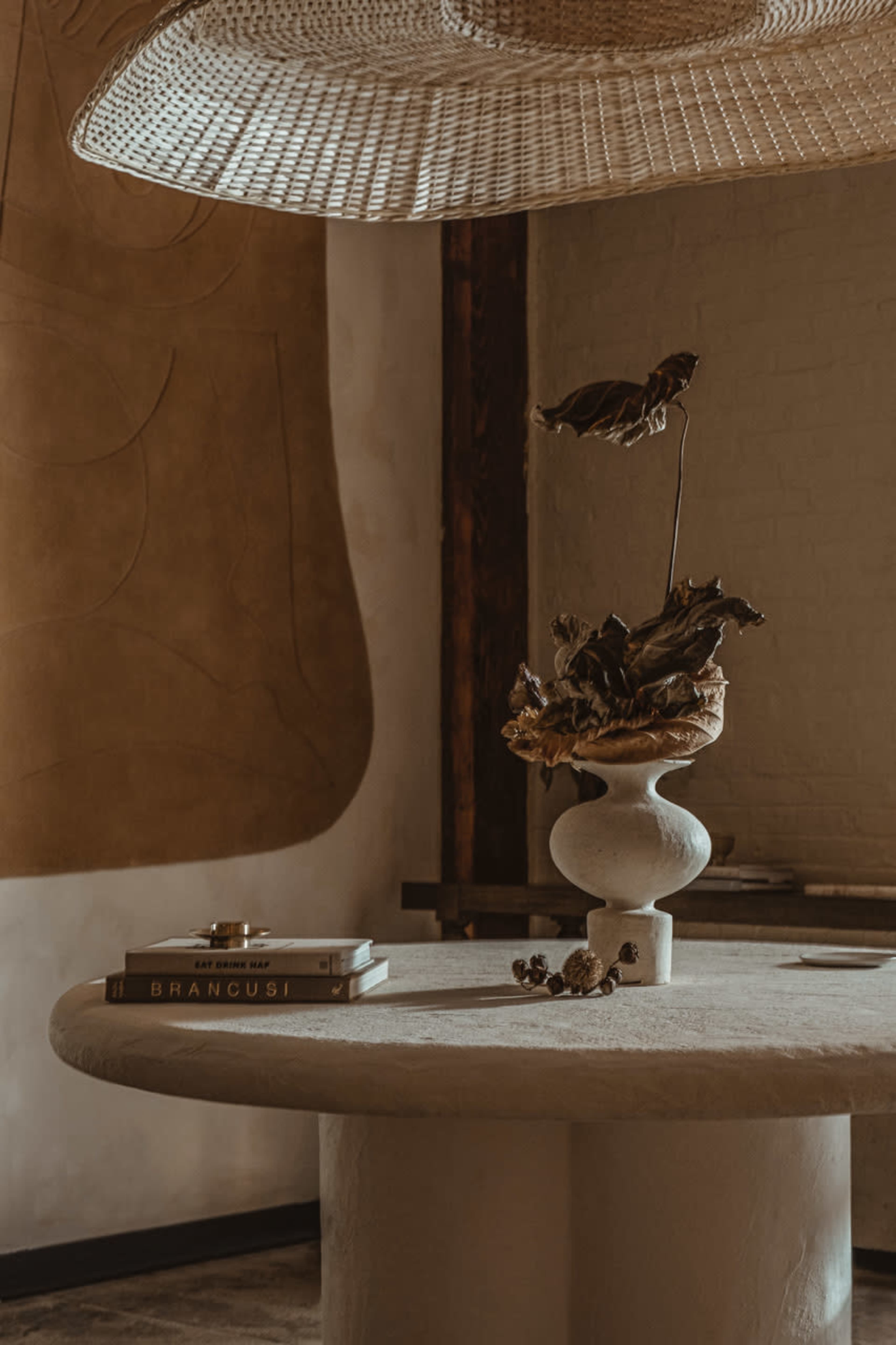 A round, textured table with a decorative vase holding dried leaves, accompanied by a book titled "Brancusi" and a small decorative object.