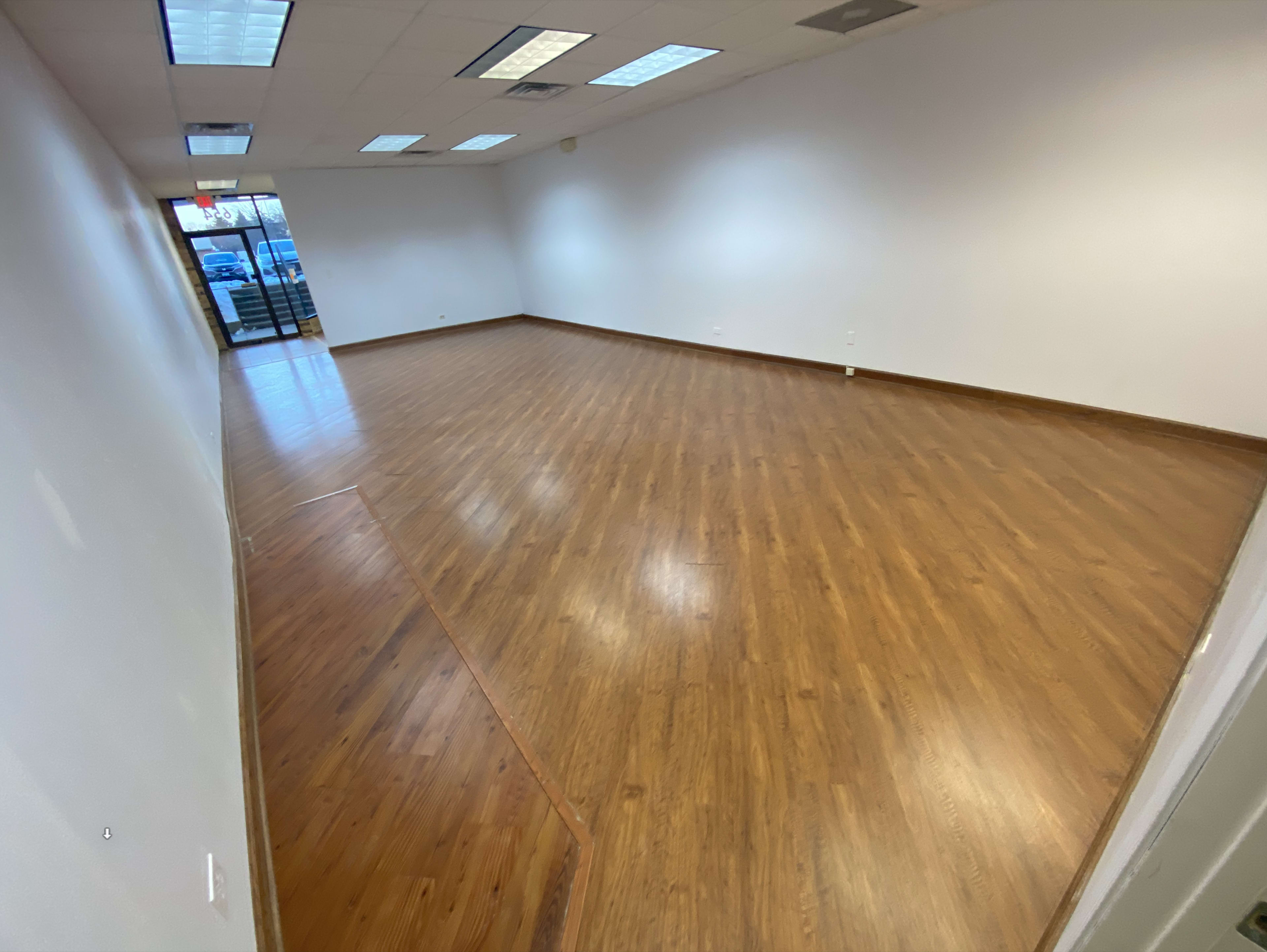 An empty room with wooden floors and white walls, featuring large windows at the entrance.