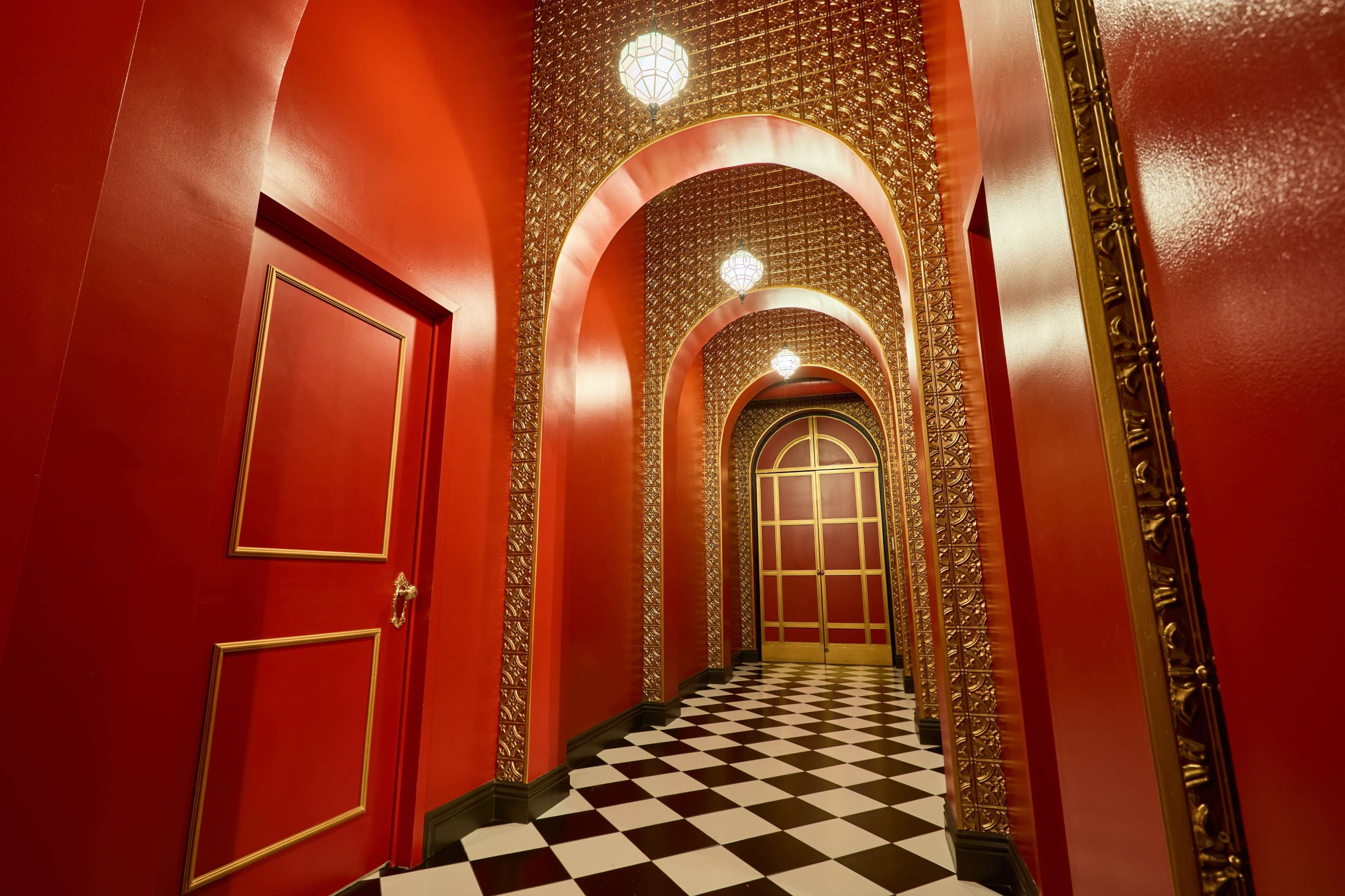 The image shows a hallway with red walls and arches, featuring gold accents and a checkered black and white floor.