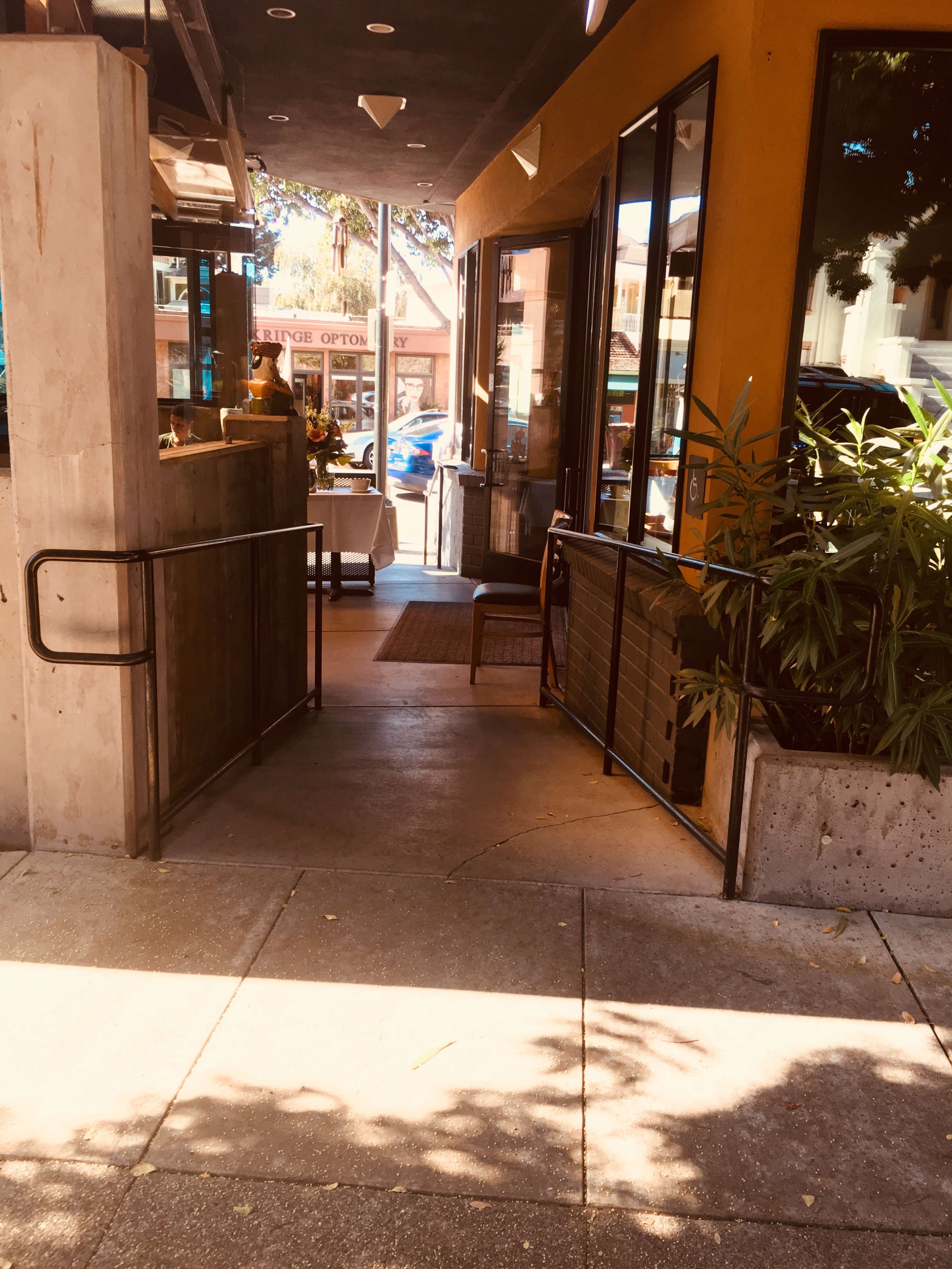 The entrance to a café, featuring an open door with a welcoming interior view and planters on the side of the walkway.