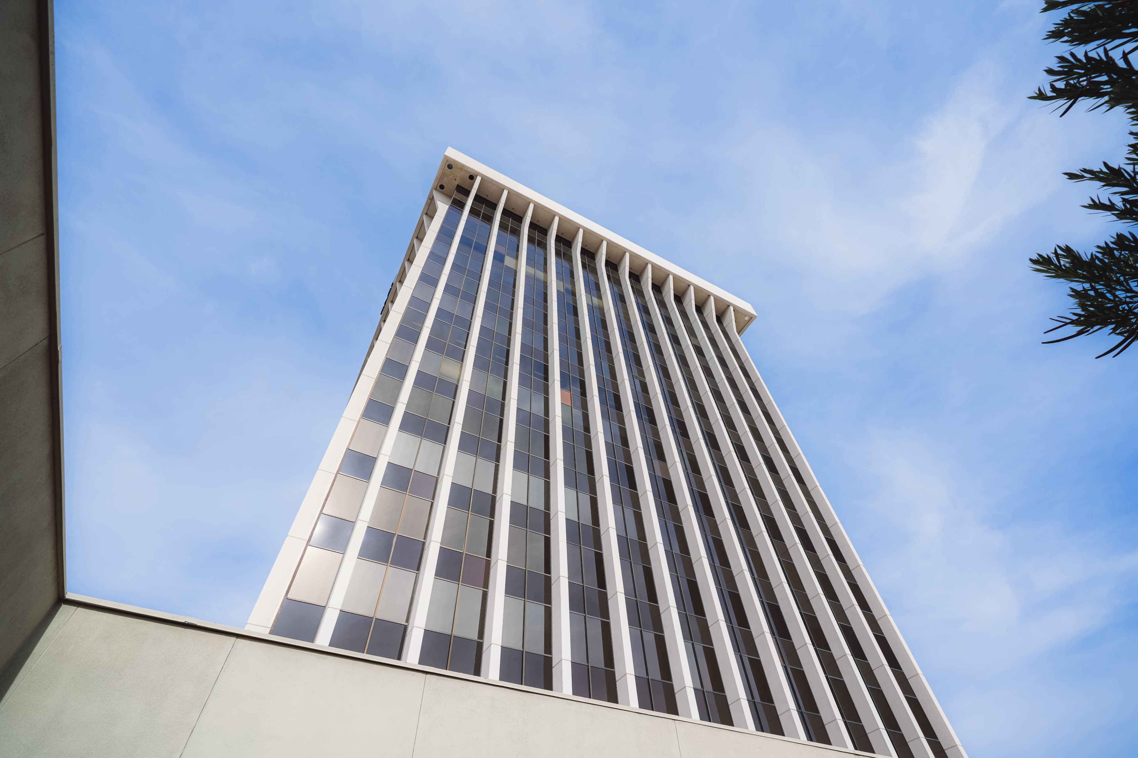 A tall commercial building with large windows and a flat roof is shown against a blue sky.