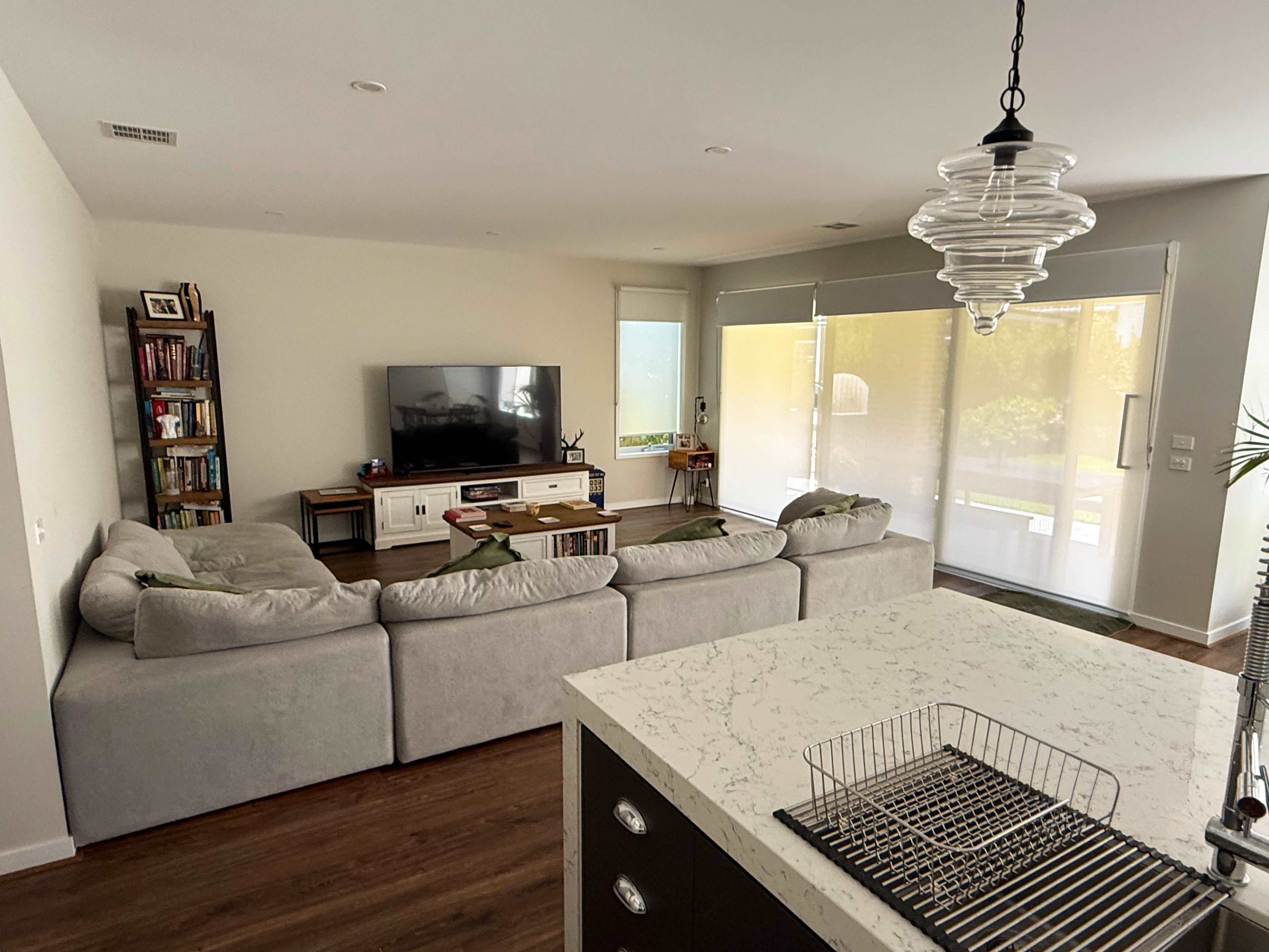 A spacious living room features a large sectional sofa, a flat-screen TV on a media console, and a dining area with a marble countertop.
