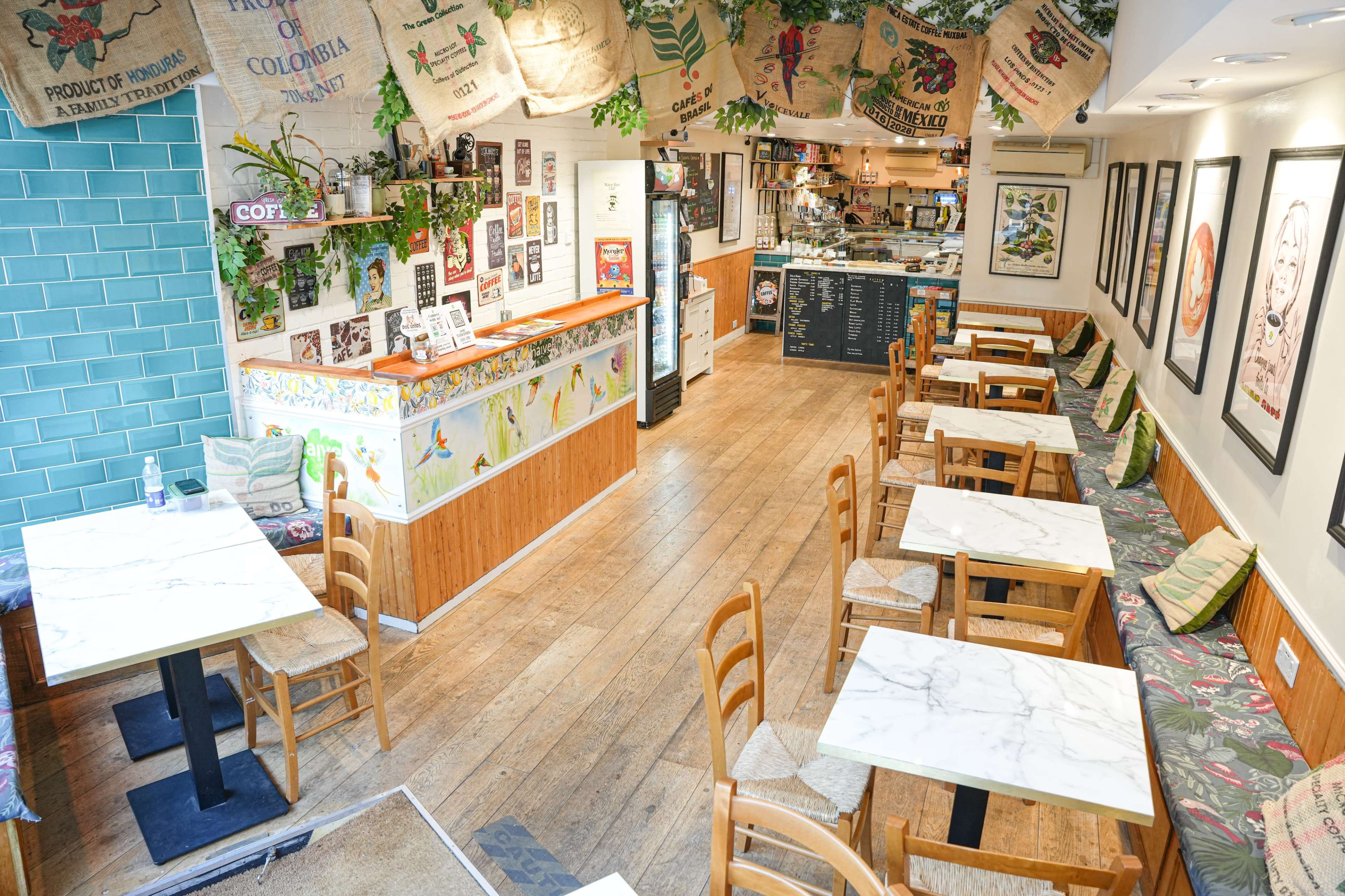 A cozy café interior with wooden floors, tables, and walls decorated with coffee-themed posters and plants.