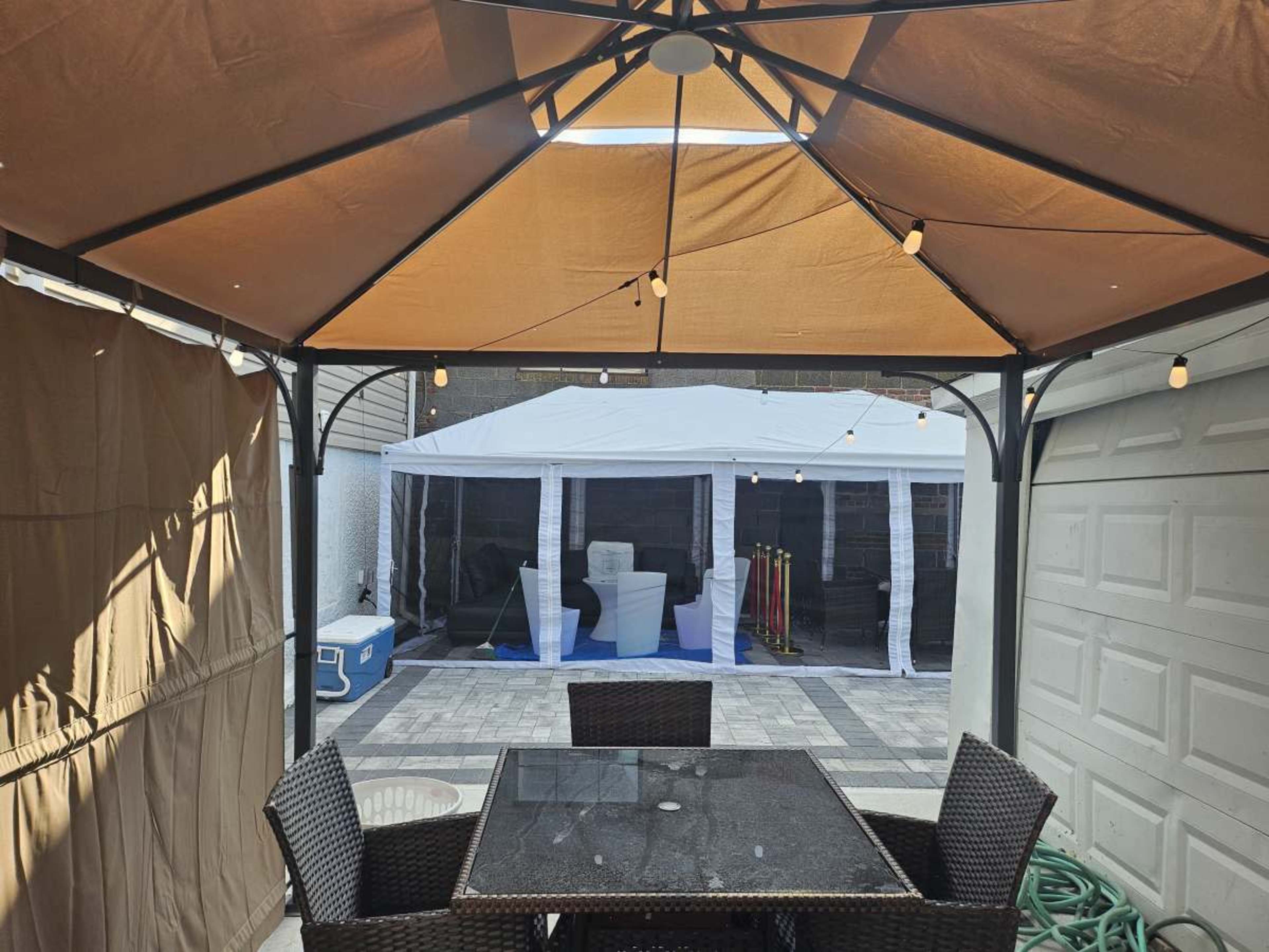 A patio gazebo with a table and chairs overlooks a tent set up in a backyard area.