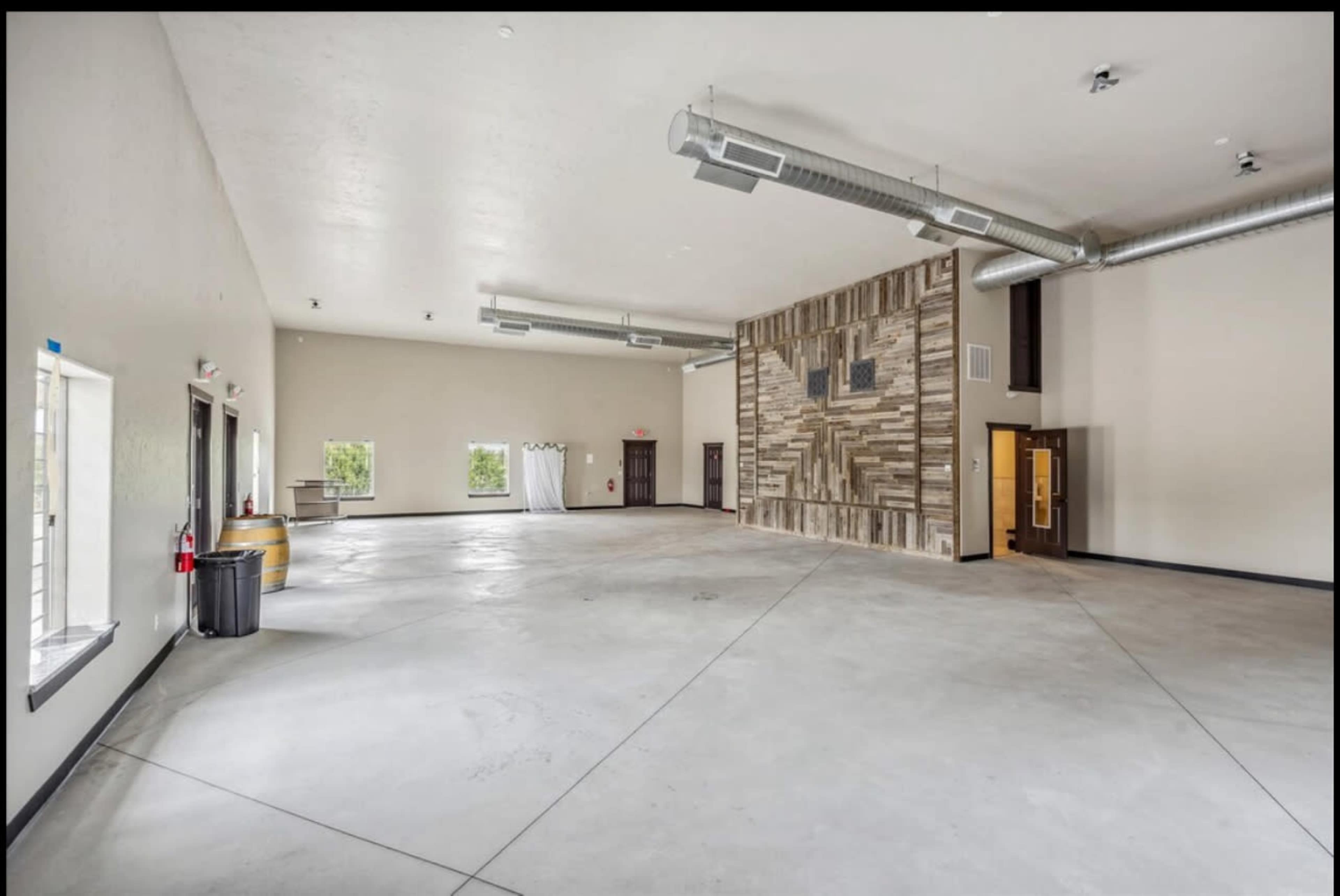 The image shows an empty, spacious interior room with light-colored walls, a polished concrete floor, and a decorated accent wall featuring wooden panels.