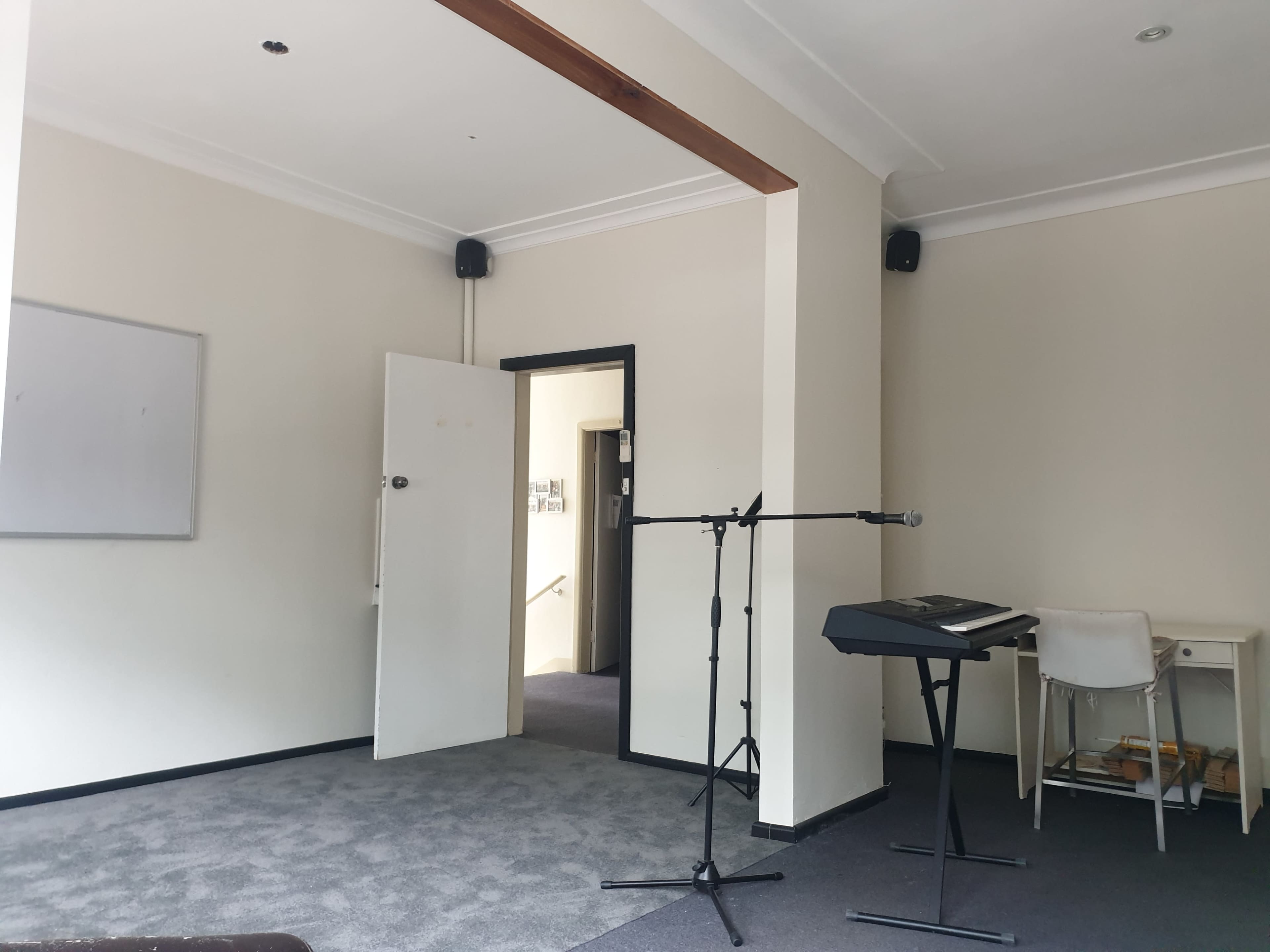 A small room features a doorway, a keyboard on a stand, a microphone, and a whiteboard mounted on the wall.