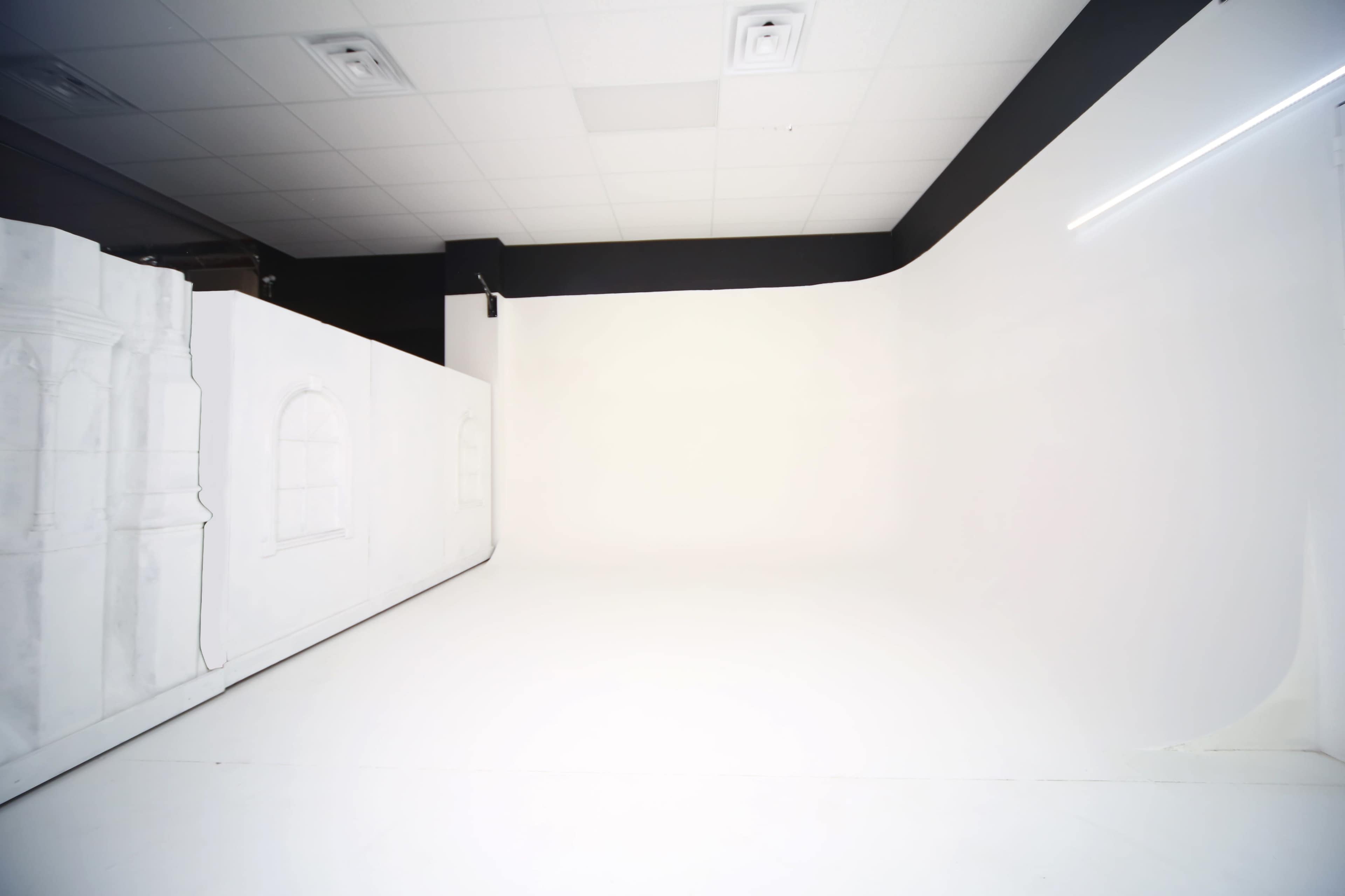The image shows a spacious photography studio with a seamless white backdrop and a painted wall featuring architectural window outlines.