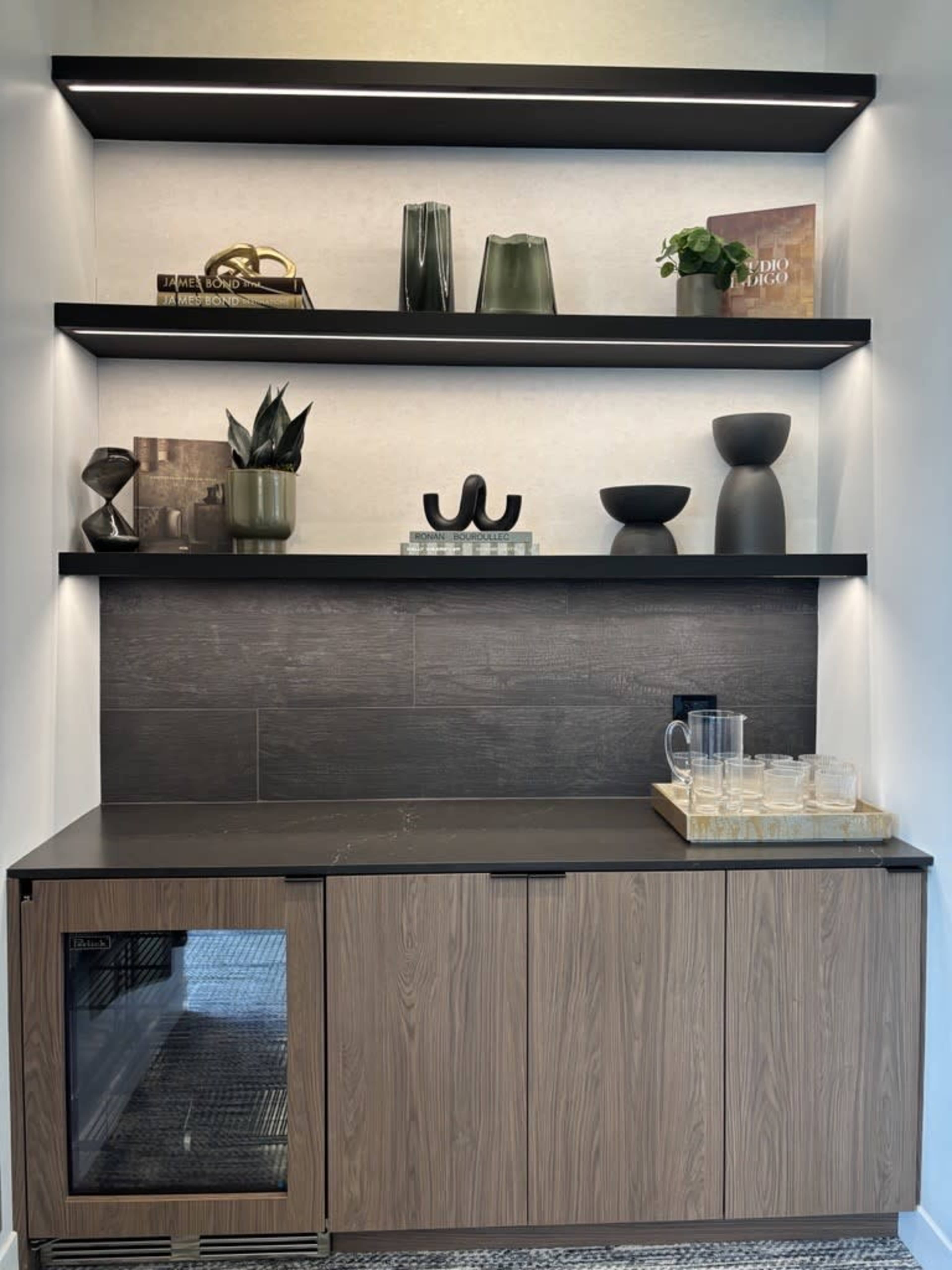 The image shows a modern cabinetry setup with a small refrigerator, decorative shelves, and various vases and plants displayed above.
