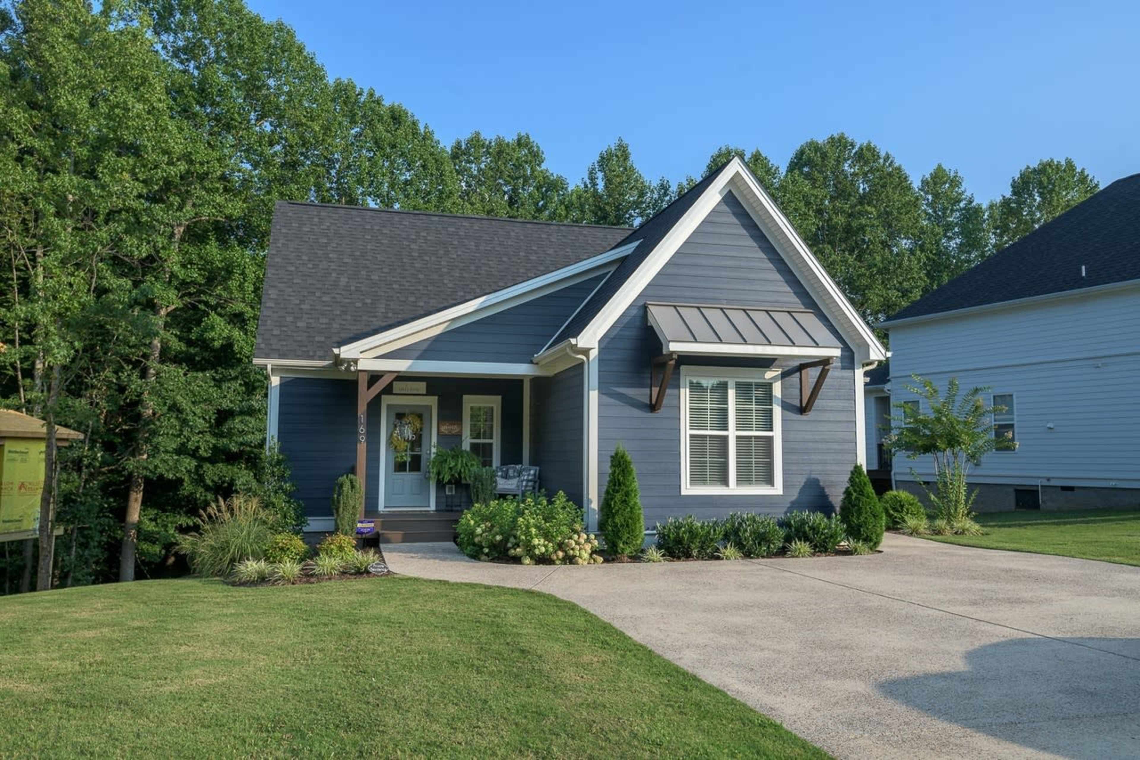 A blue house with a peaked roof and a front porch is surrounded by a well-maintained lawn and landscaping.