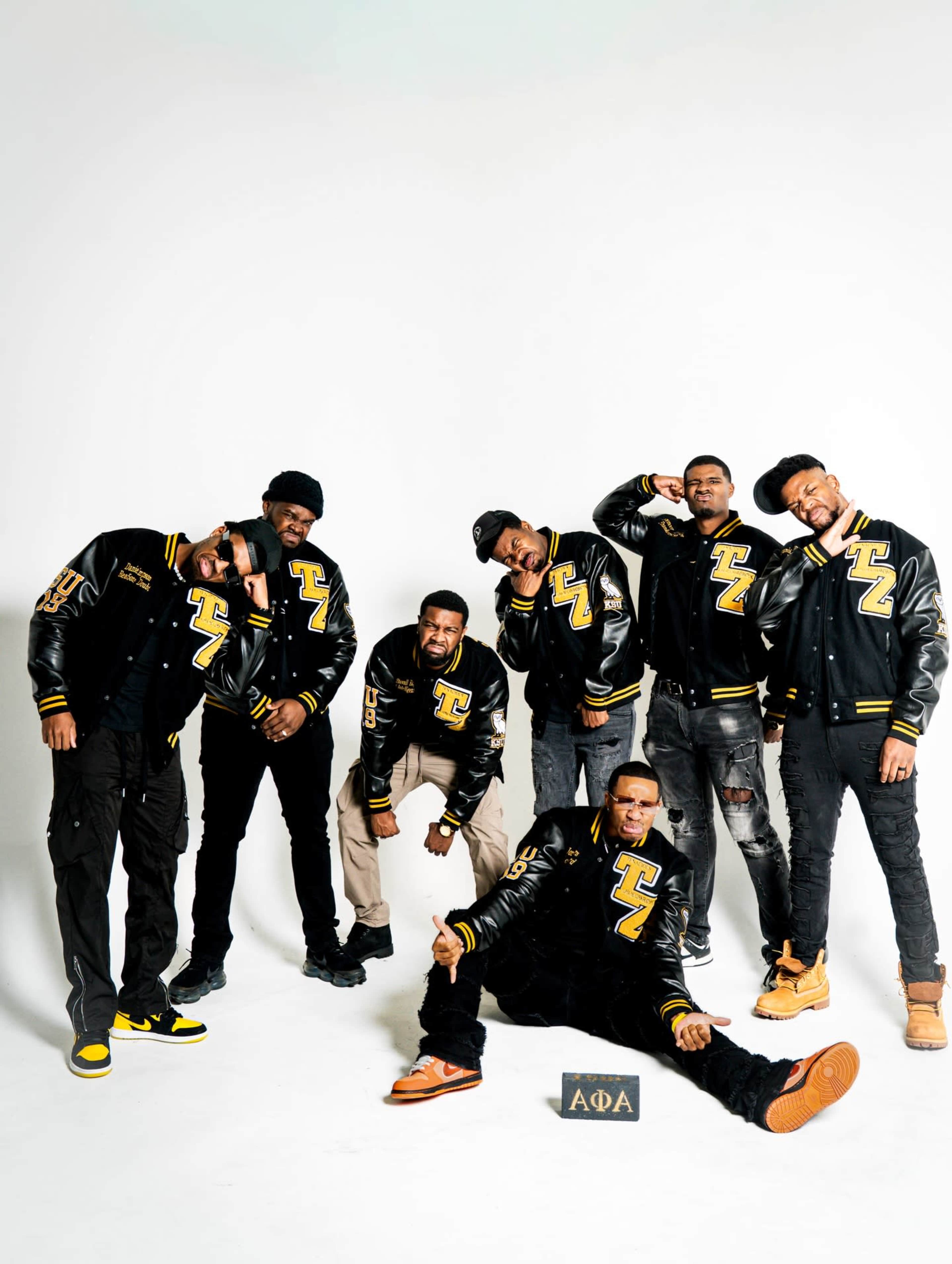A group of six men poses together, wearing black and yellow varsity jackets, with a sign that reads "ΑΦΑ" in the foreground.