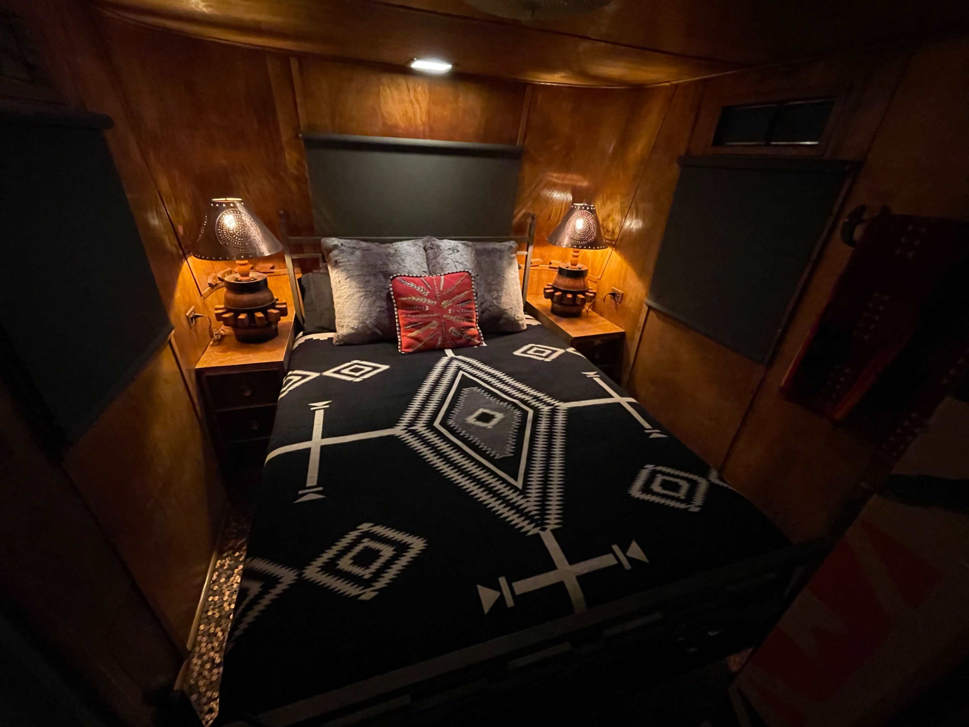 The image shows a cozy bedroom with a bed covered in a patterned black and white blanket, flanked by two bedside lamps.