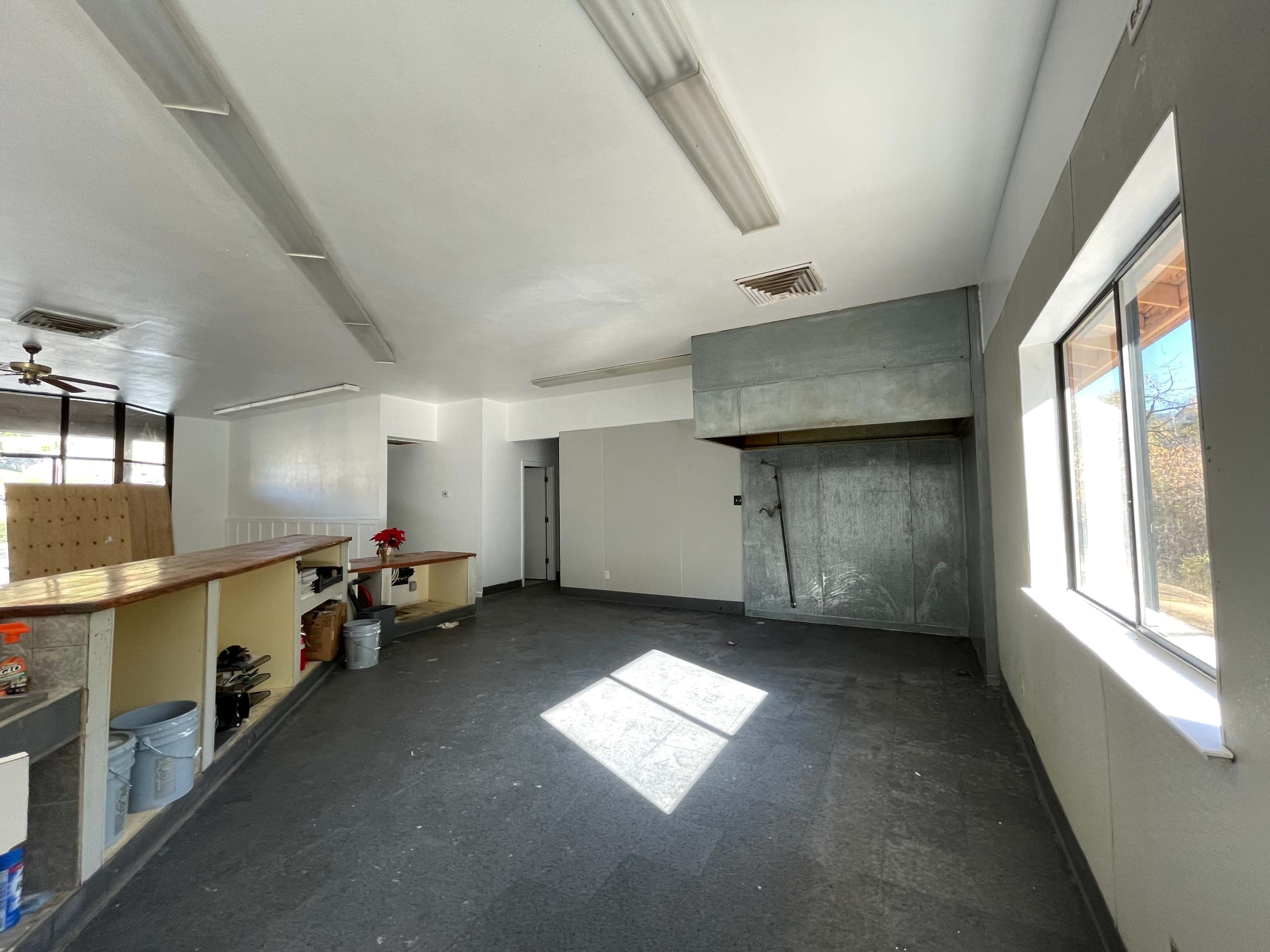 An empty room with gray walls, a large window, and a metal exhaust hood in one corner.