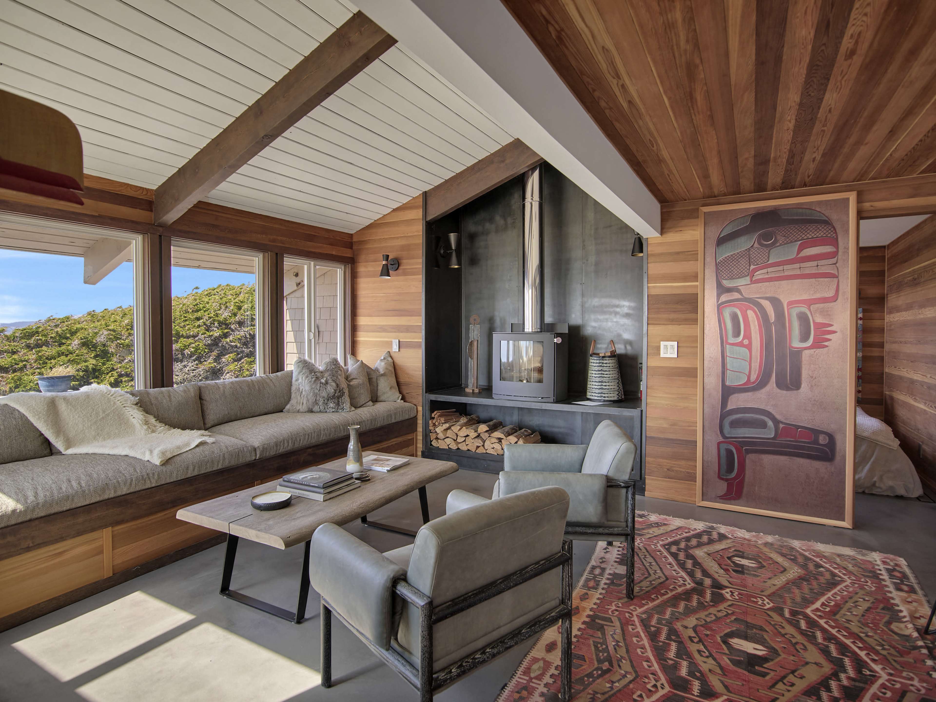 The living area features a modern design with a large sectional sofa, a central coffee table, and a wood-burning stove set against wooden paneling, alongside a decorative wall graphic.