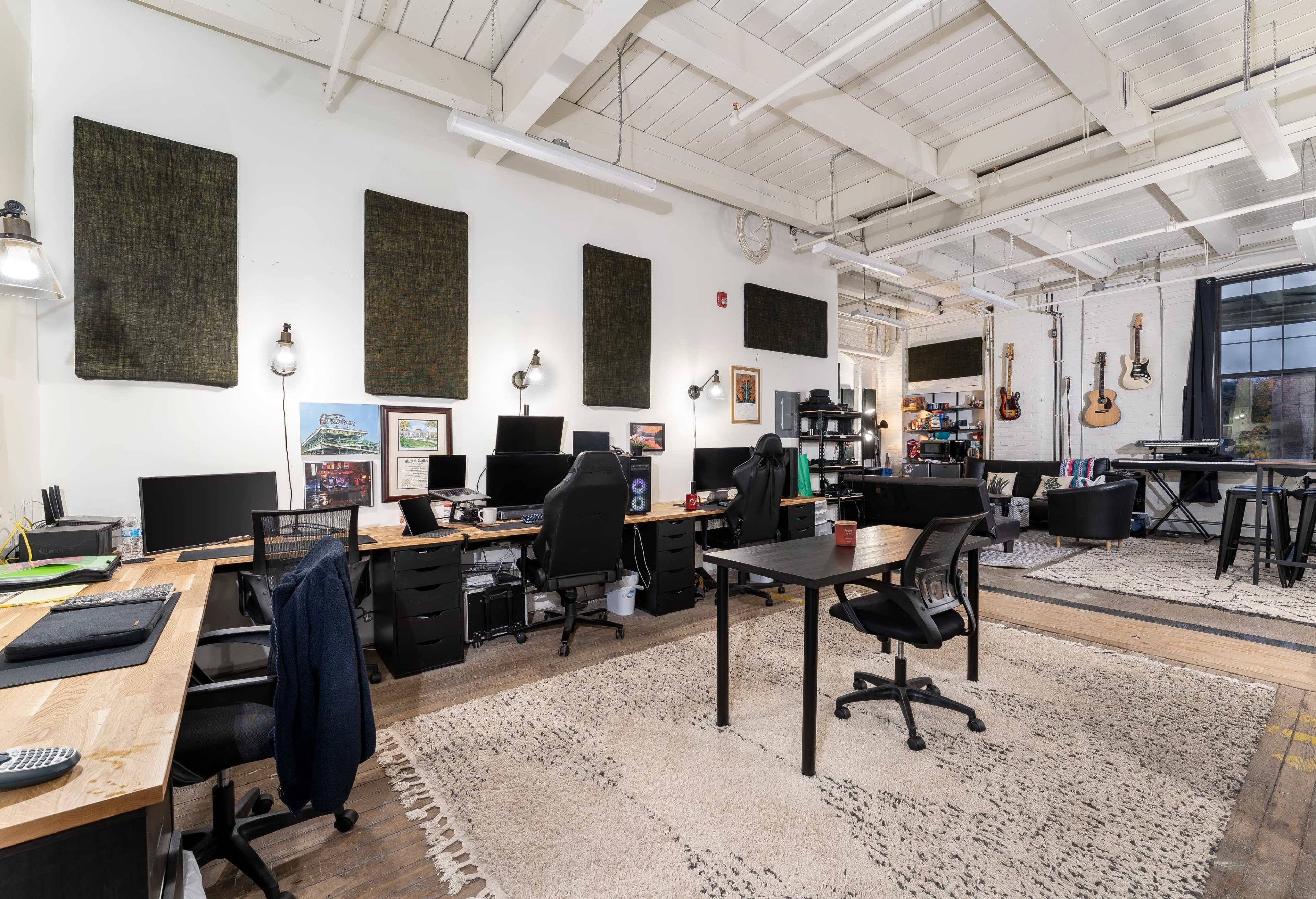 A spacious office with multiple workstations, black chairs, and musical instruments hanging on the walls.