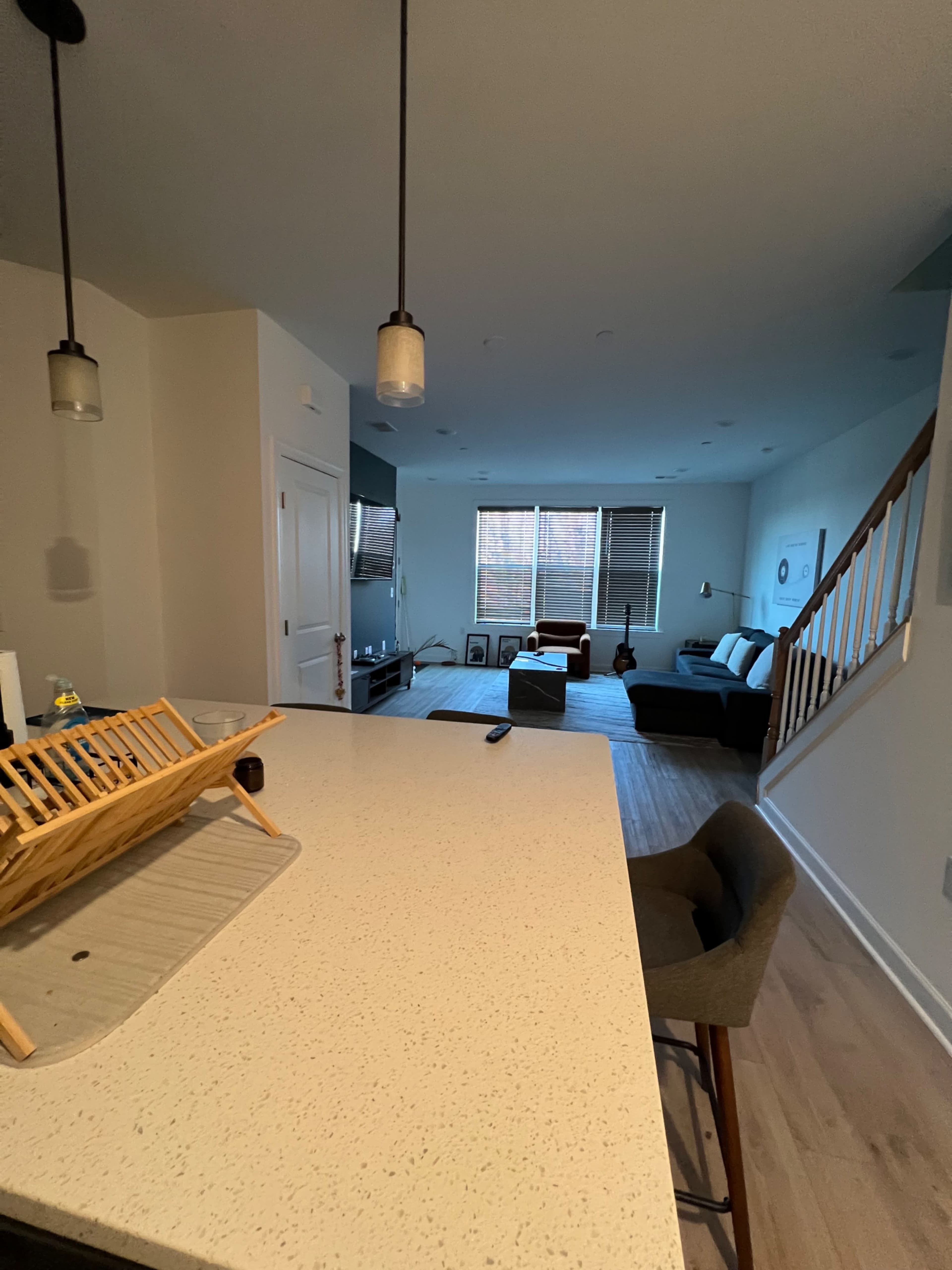 The image shows a modern, open-concept living room with a kitchen counter in the foreground, featuring a seating area and a guitar leaning against the wall.