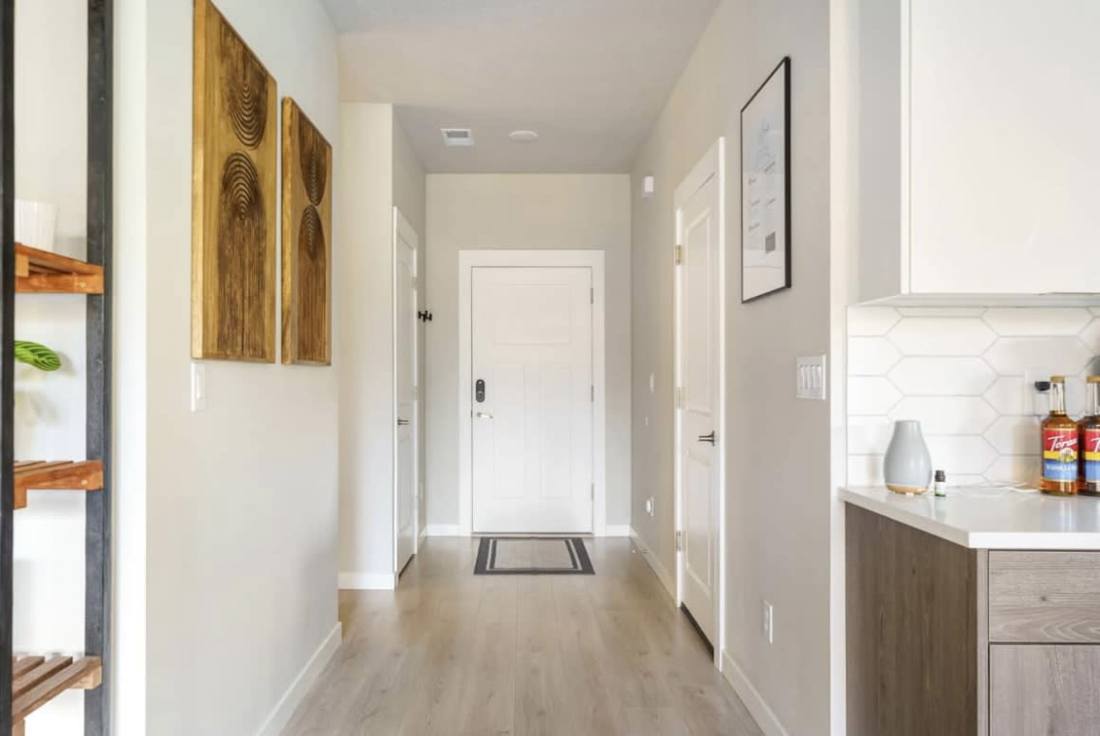 A modern hallway features a light-colored floor, simple decor, and a closed door at the end.