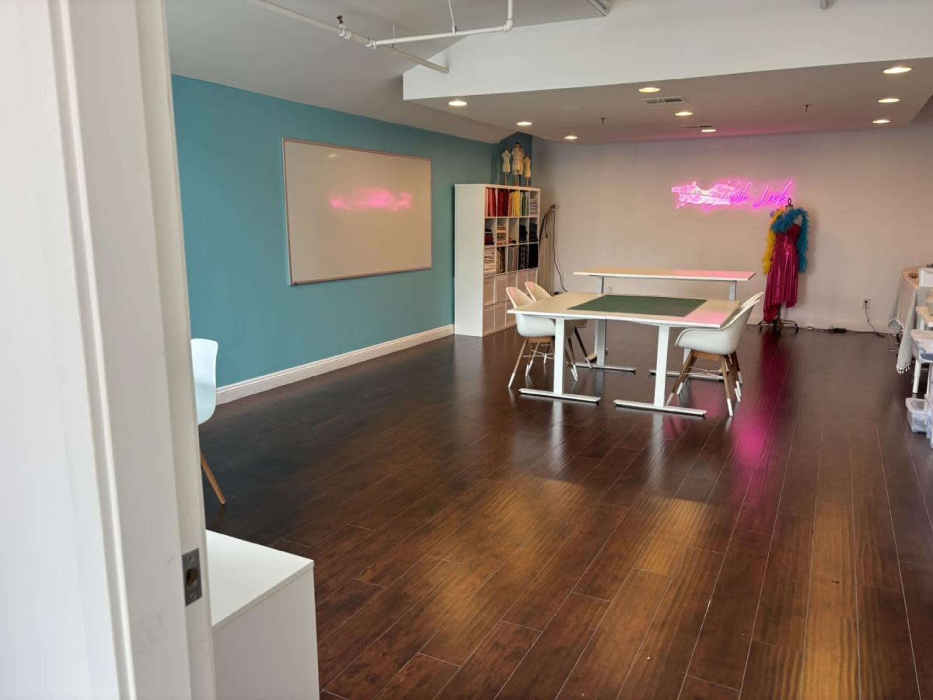 The image shows a spacious, brightly lit room with a table and chairs, a whiteboard on the wall, and colorful decor.