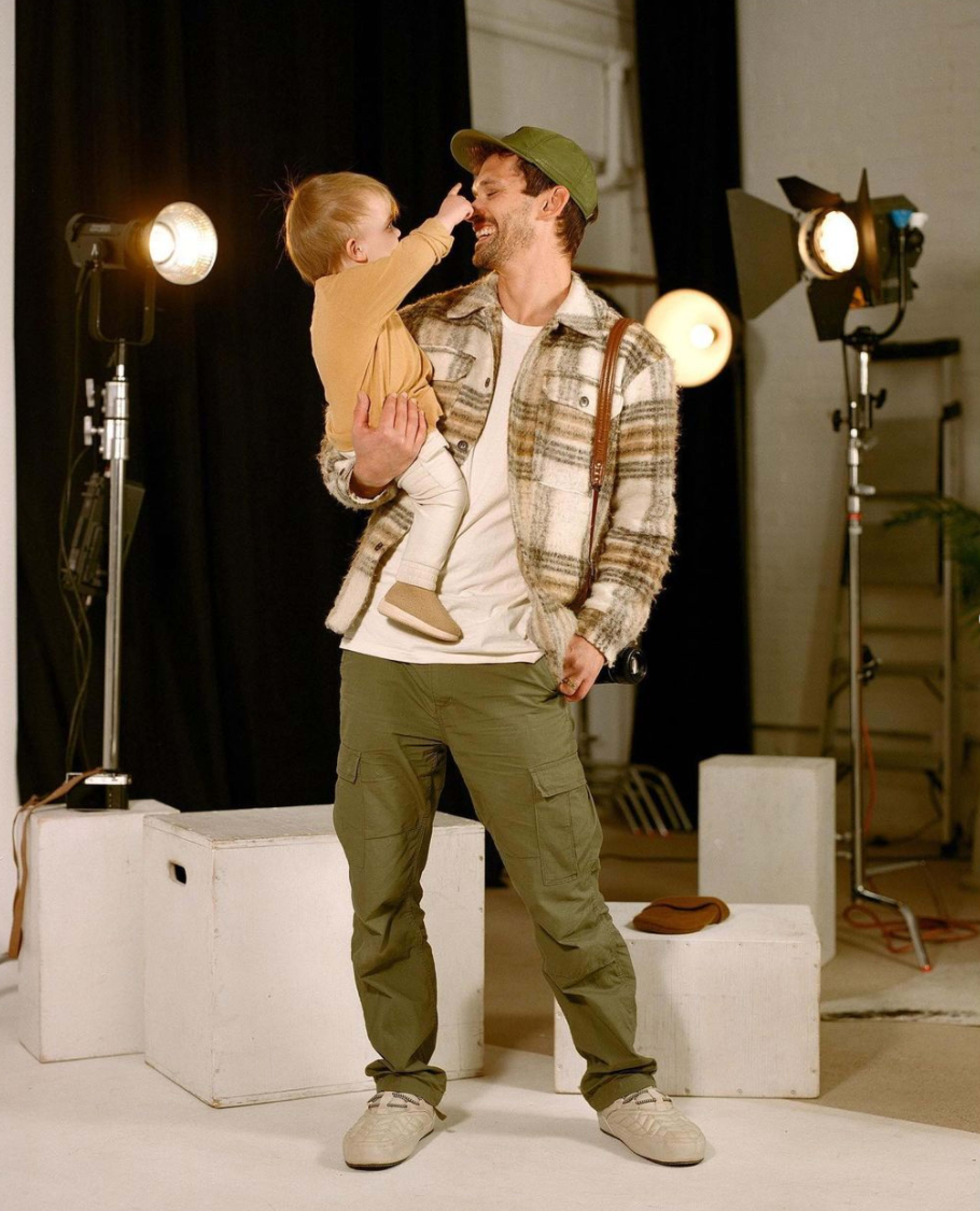 A man holds a toddler while smiling at each other, surrounded by studio lighting and equipment.