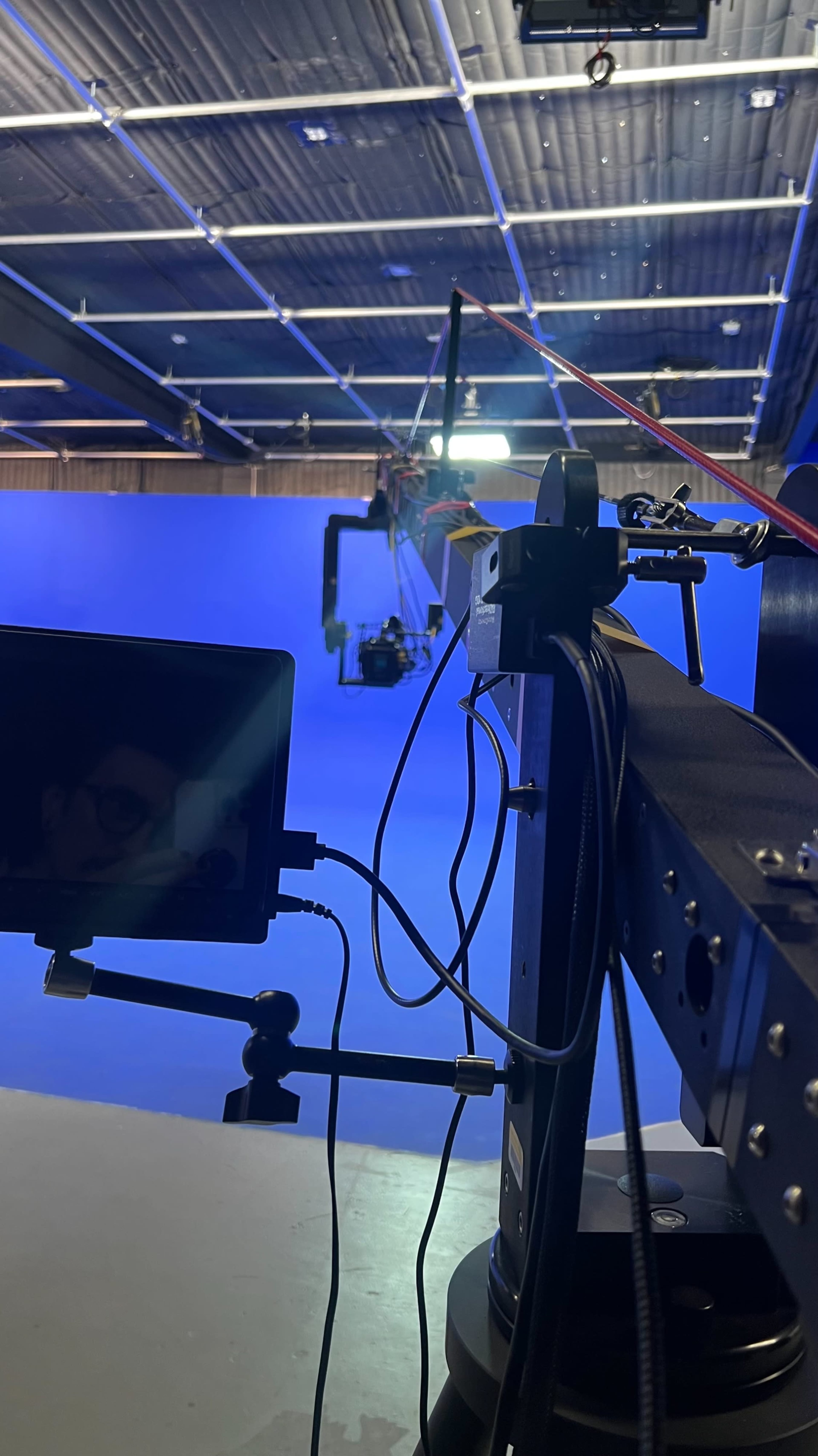 A film production setup with a camera mounted on a crane and a blue backdrop.