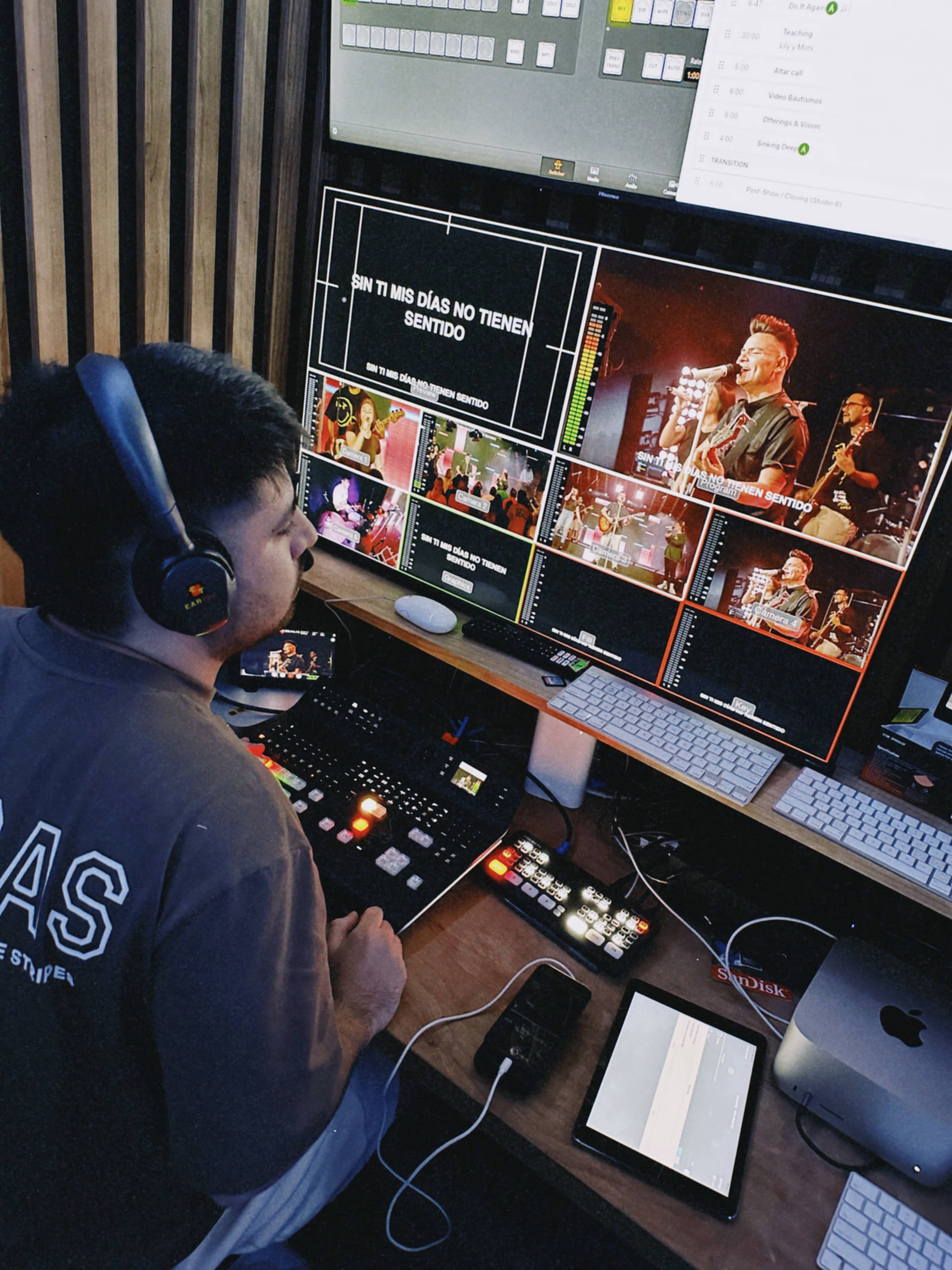 A person operates equipment in a broadcast control room, monitoring multiple screens displaying video feeds and text.