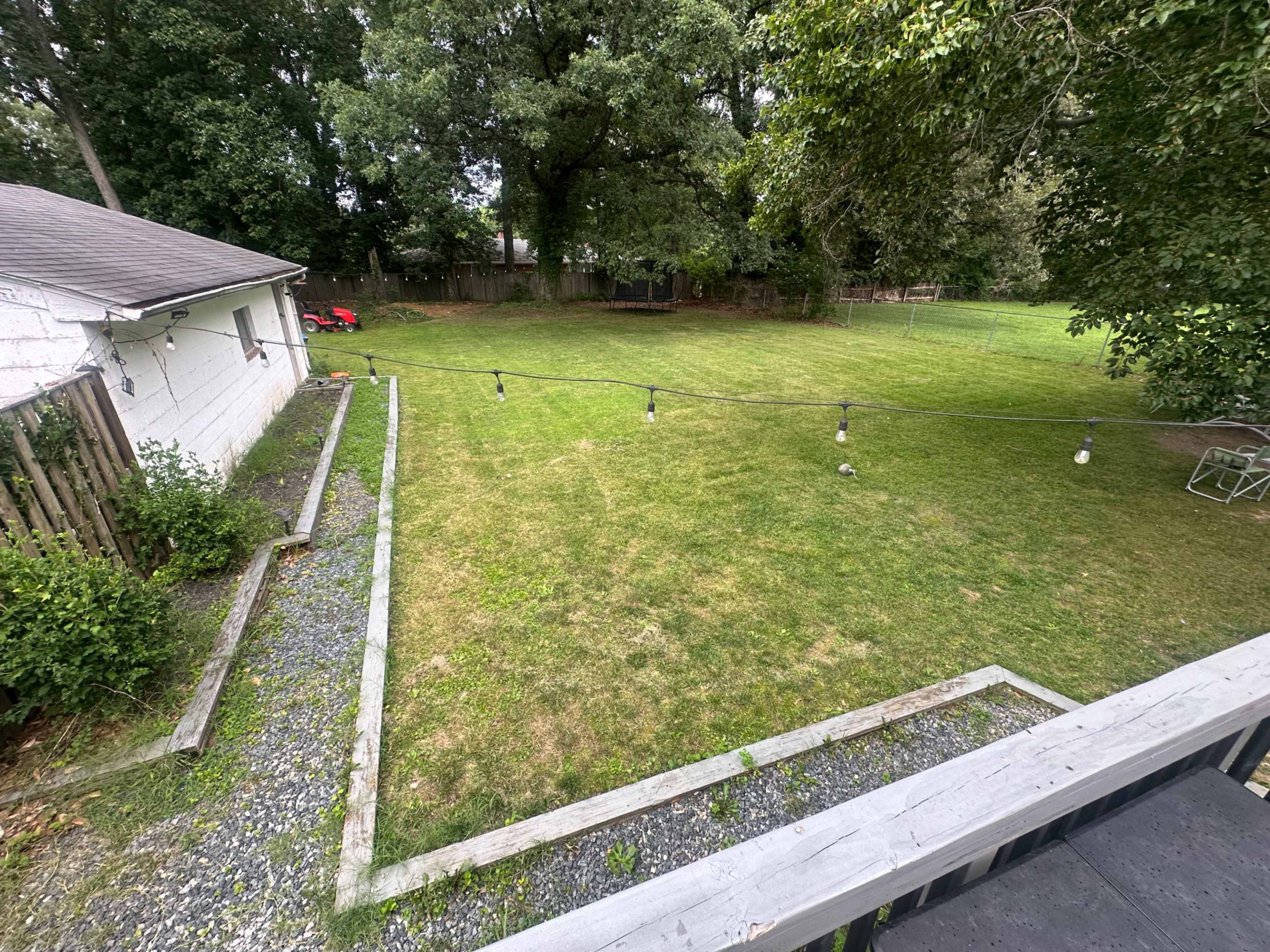 The image shows a spacious, grassy backyard with a house on one side and a string of lights hanging above.