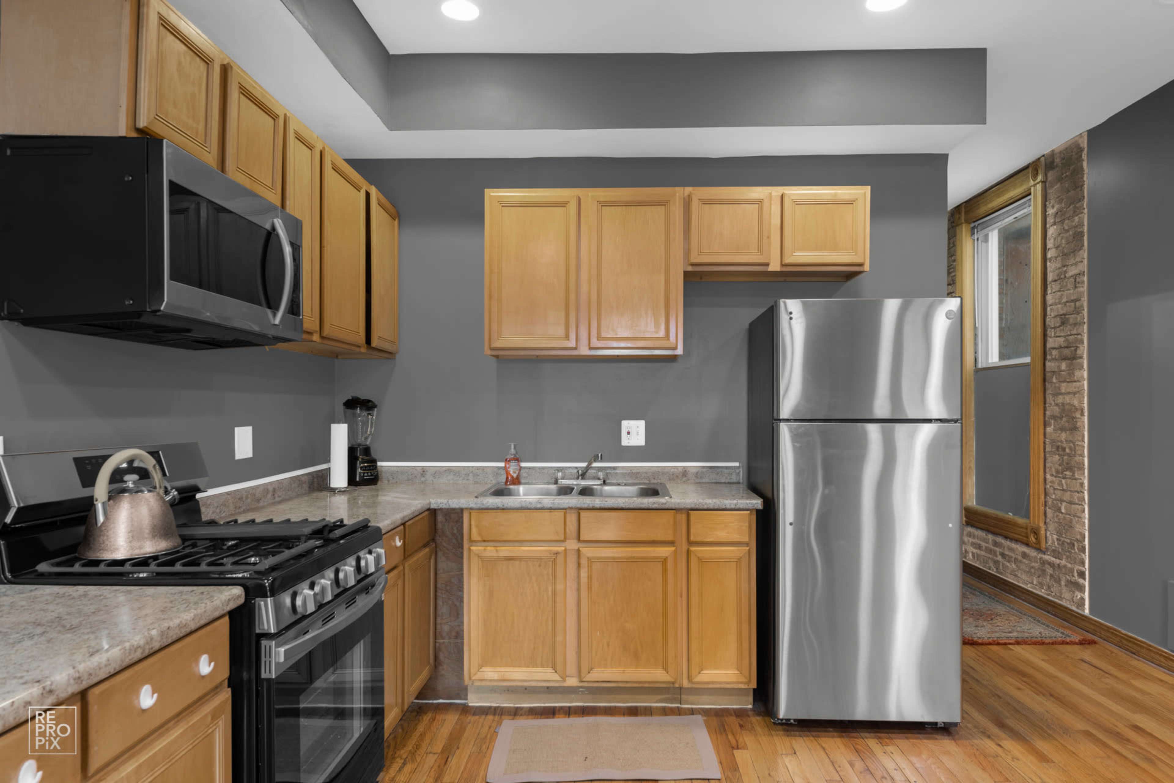 The kitchen features wooden cabinets, stainless steel appliances, and a countertop with a sink against a gray wall.