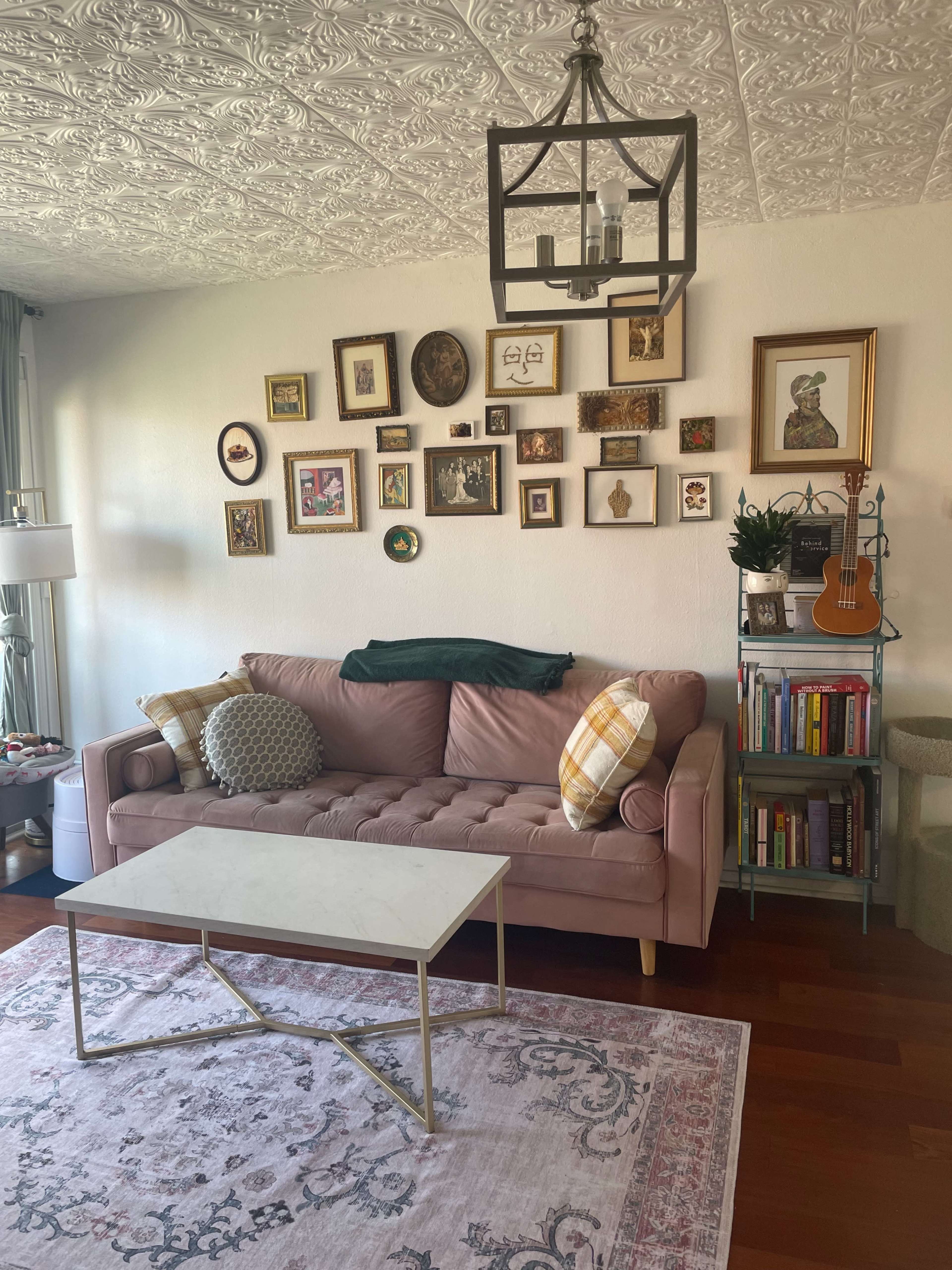 A pink sofa is placed against a wall adorned with various framed artworks, accompanied by a coffee table and a bookshelf filled with books.