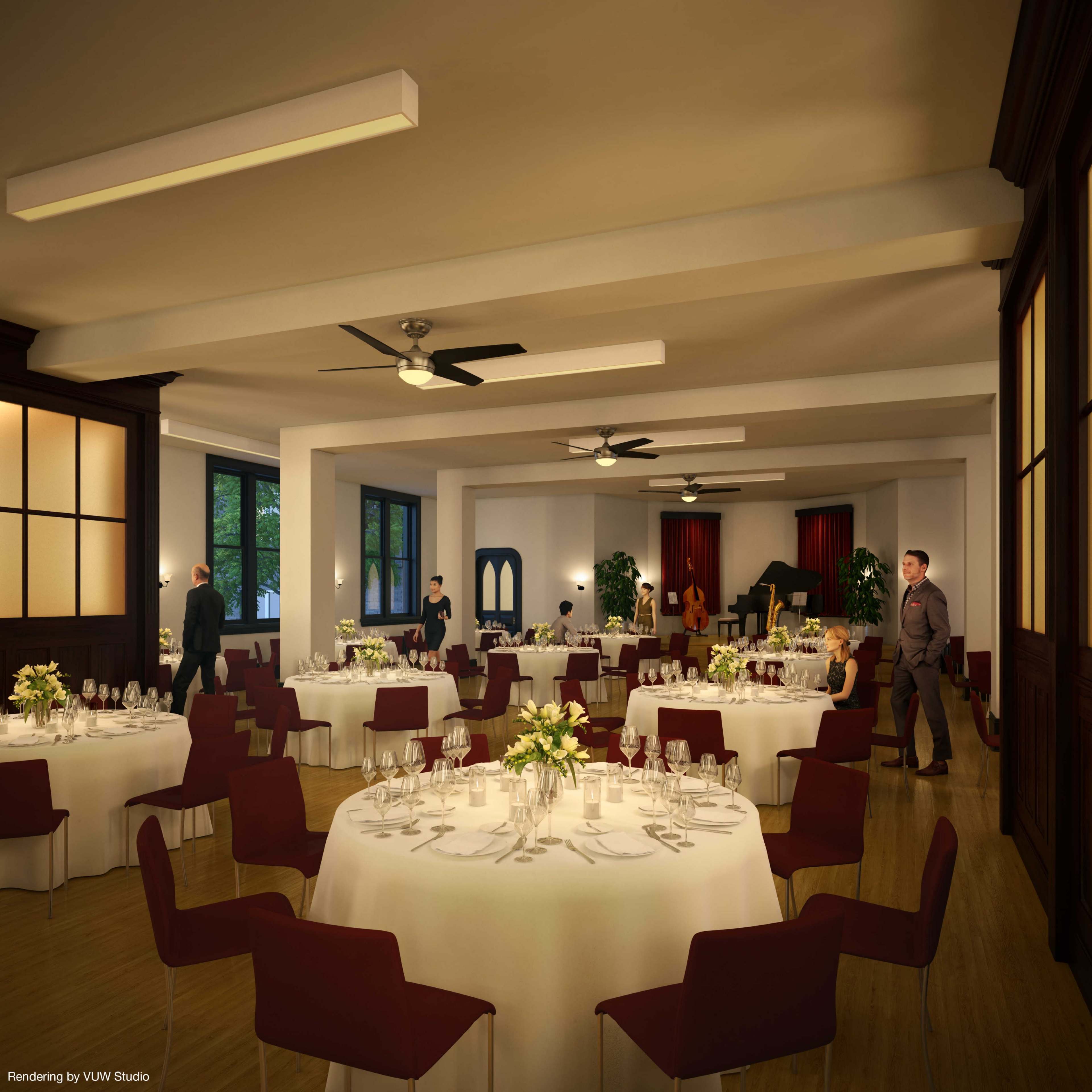 A spacious dining area features round tables set with white tablecloths, elegant centerpieces, and guests mingling in a well-lit room with large windows.