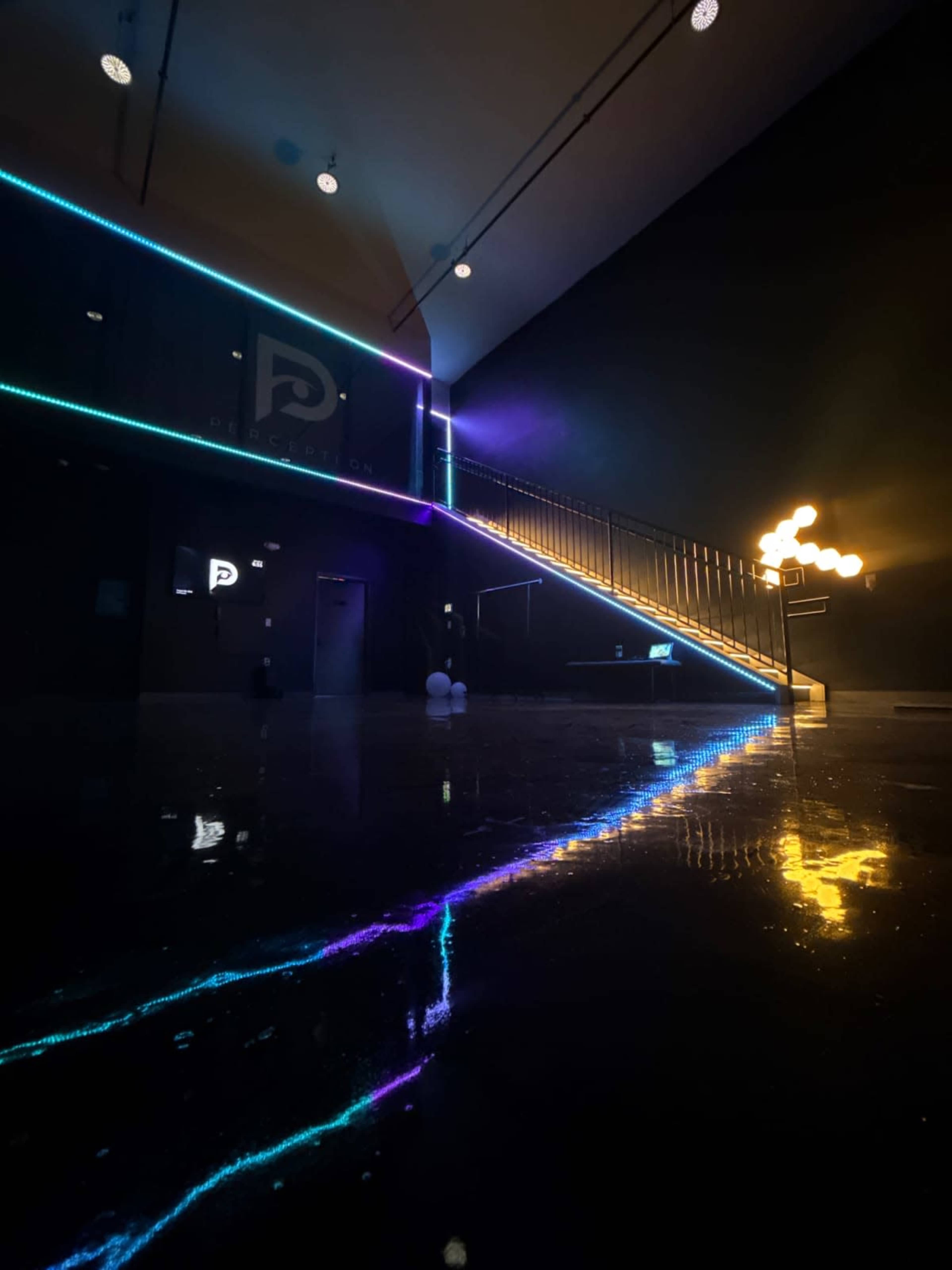 The image shows a modern interior space featuring a staircase illuminated with colorful LED light strips and a glossy, reflective floor.