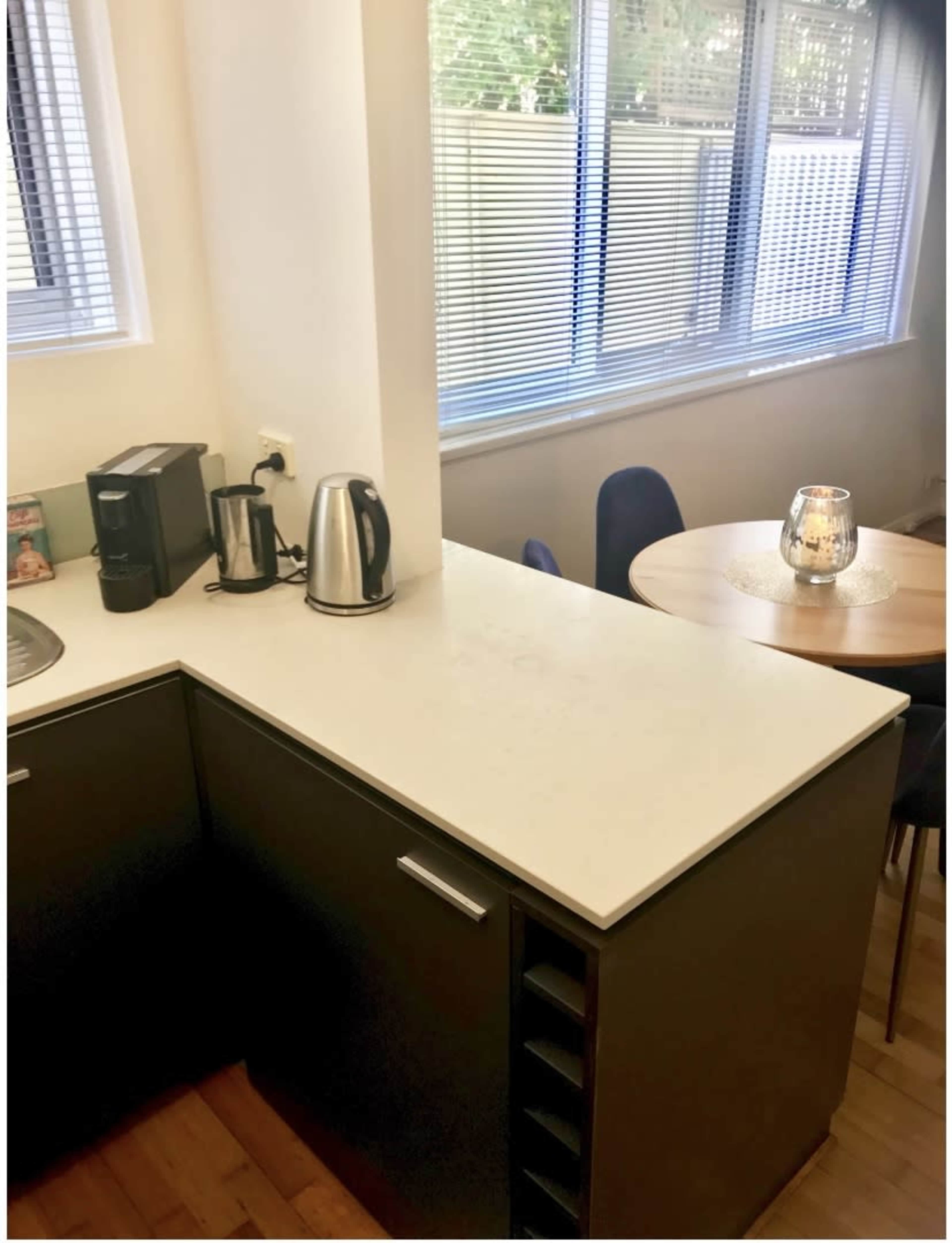 A kitchen corner with a coffee maker and kettle on a countertop, alongside a dining area featuring a round table and chairs.