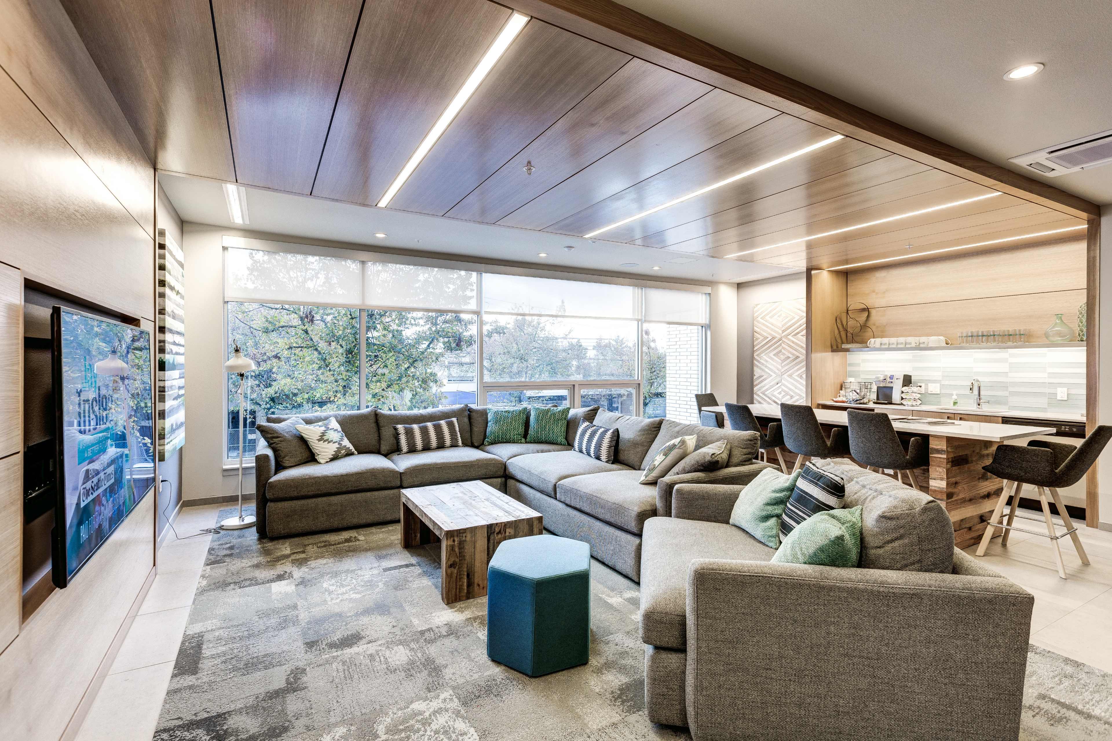 A modern living room with a large sectional sofa, a coffee table, and a dining area in the background, featuring natural light from large windows.