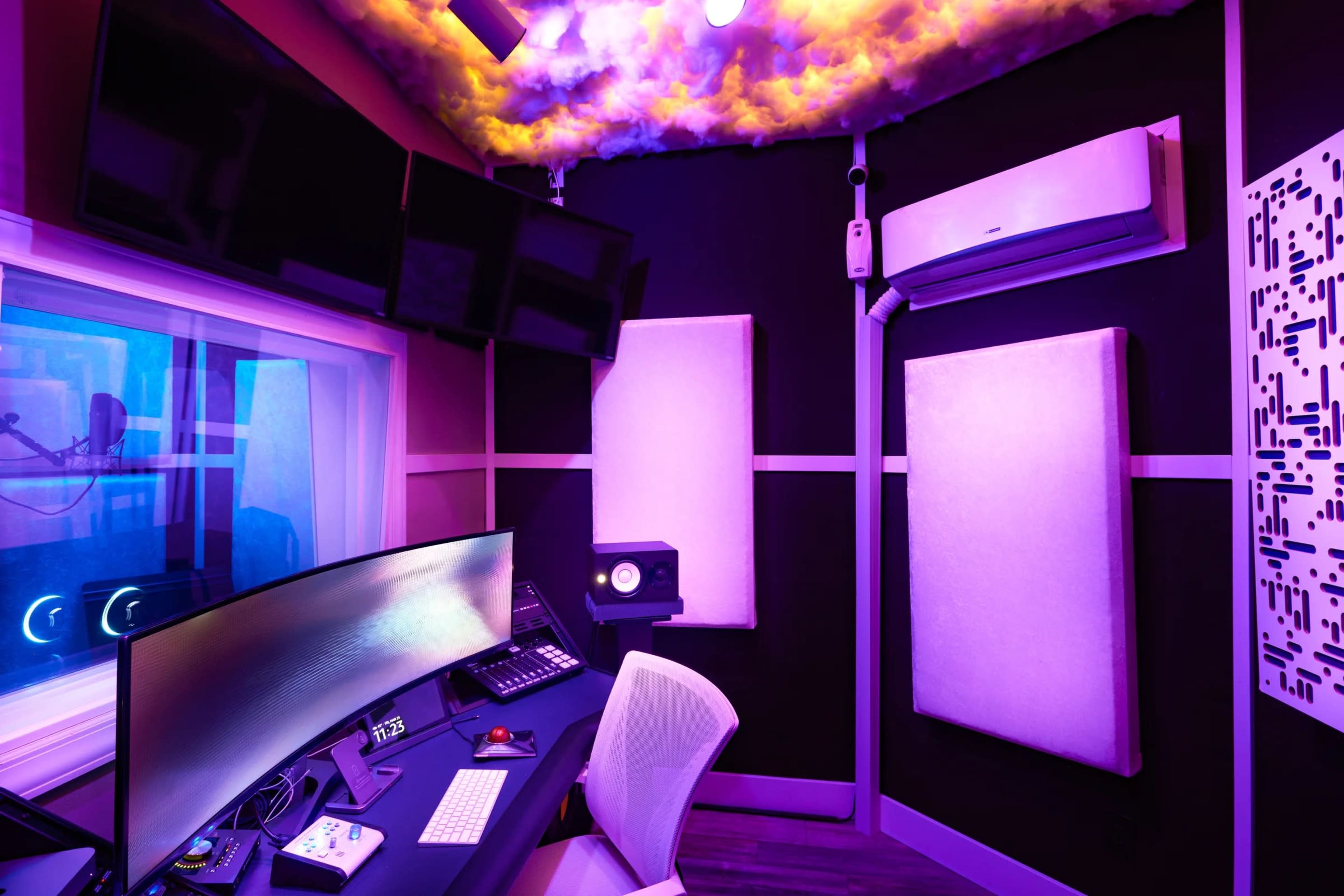A modern music studio with multiple screens, sound panels, and colorful lighting.
