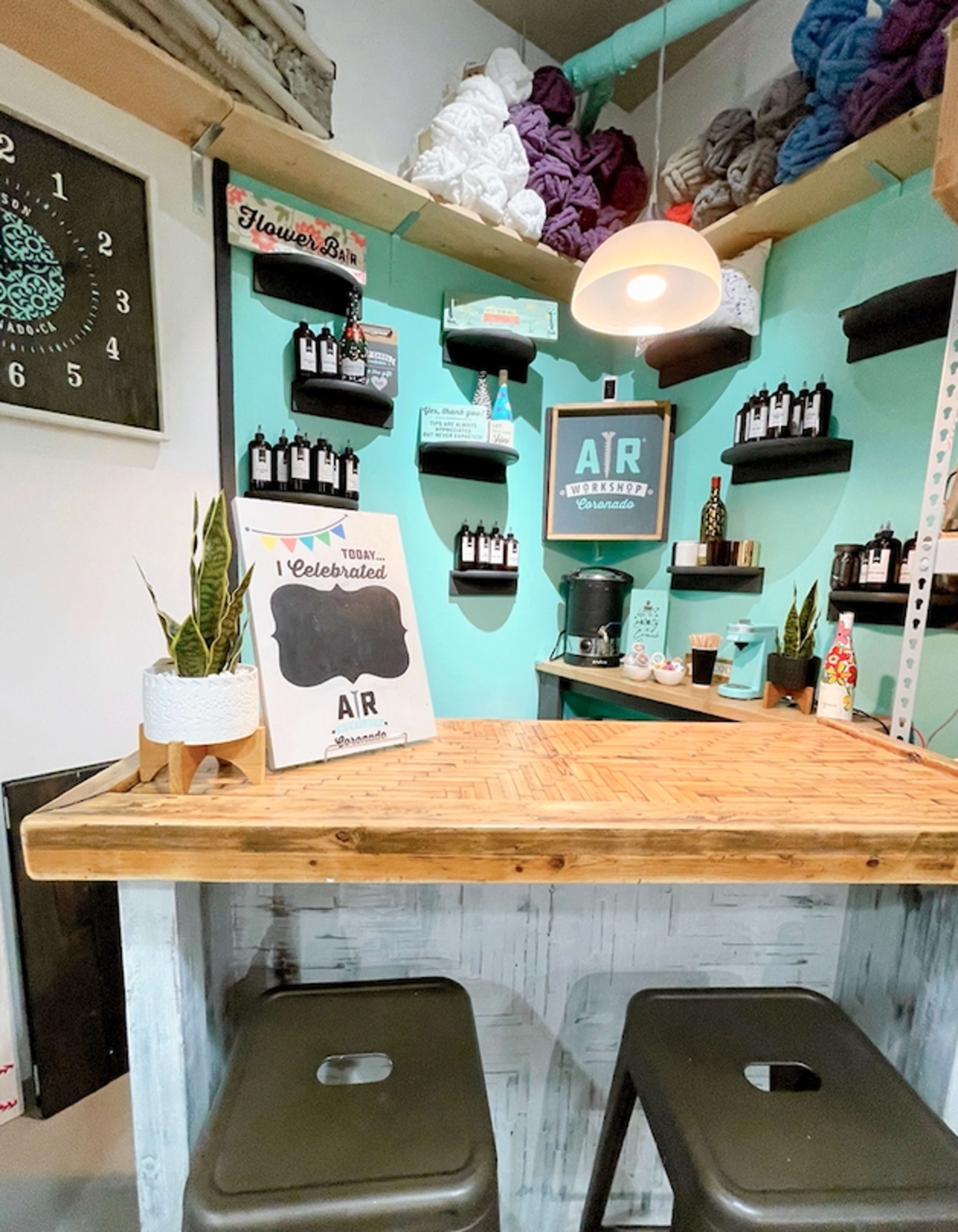 A cozy, well-organized space with a wooden counter, shelves displaying various bottles and decorative items, and a coffee maker against a mint green wall.