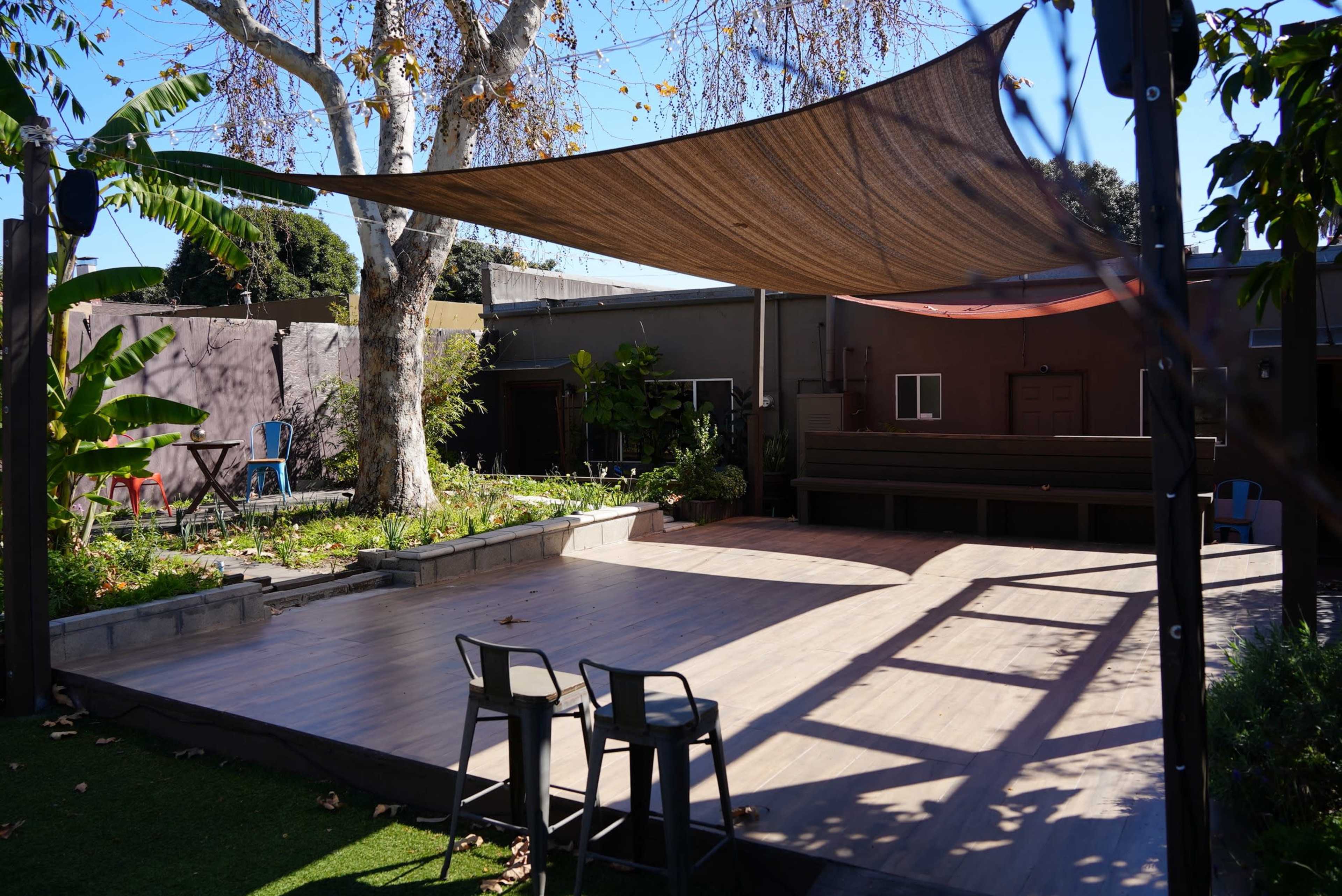An outdoor space with a wooden deck, a shaded area created by a large canopy, and surrounding greenery.
