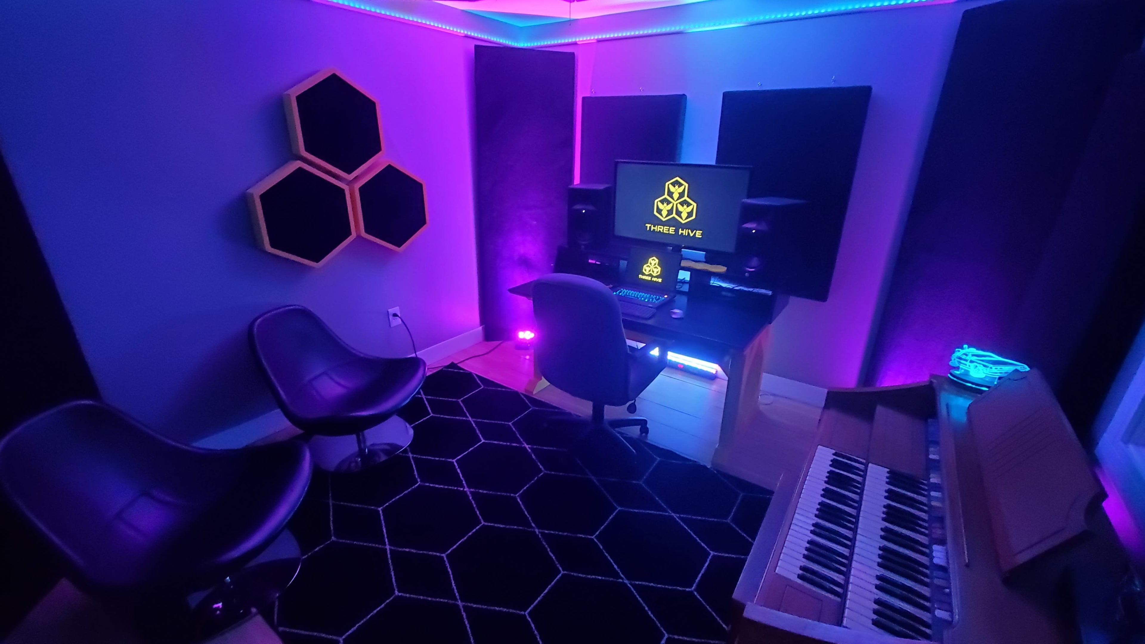 A modern music studio features stylish seating, a keyboard, and colorful LED lighting.