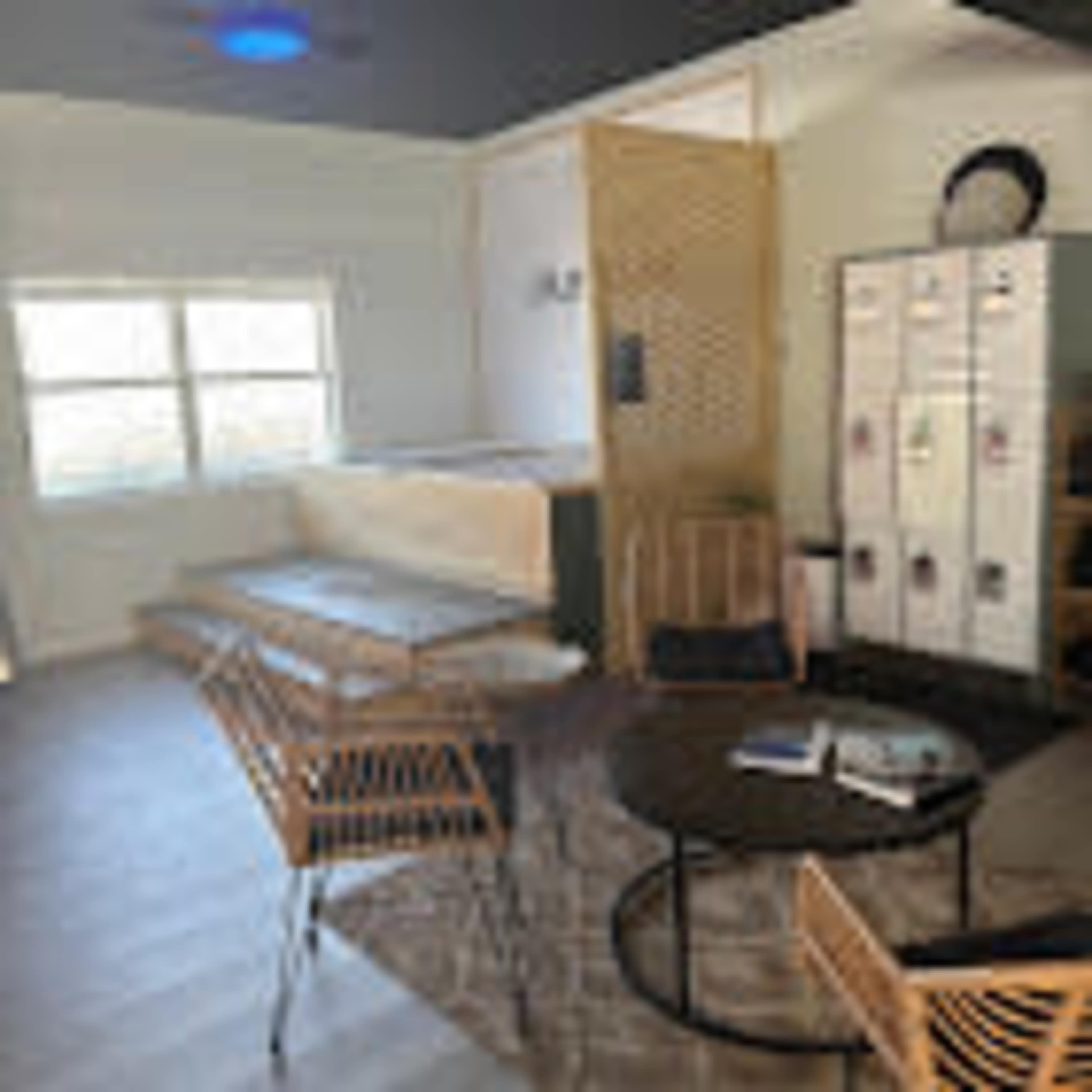 The image shows a modern, casual lounge area featuring wooden benches, lockers, and a round table with chairs.