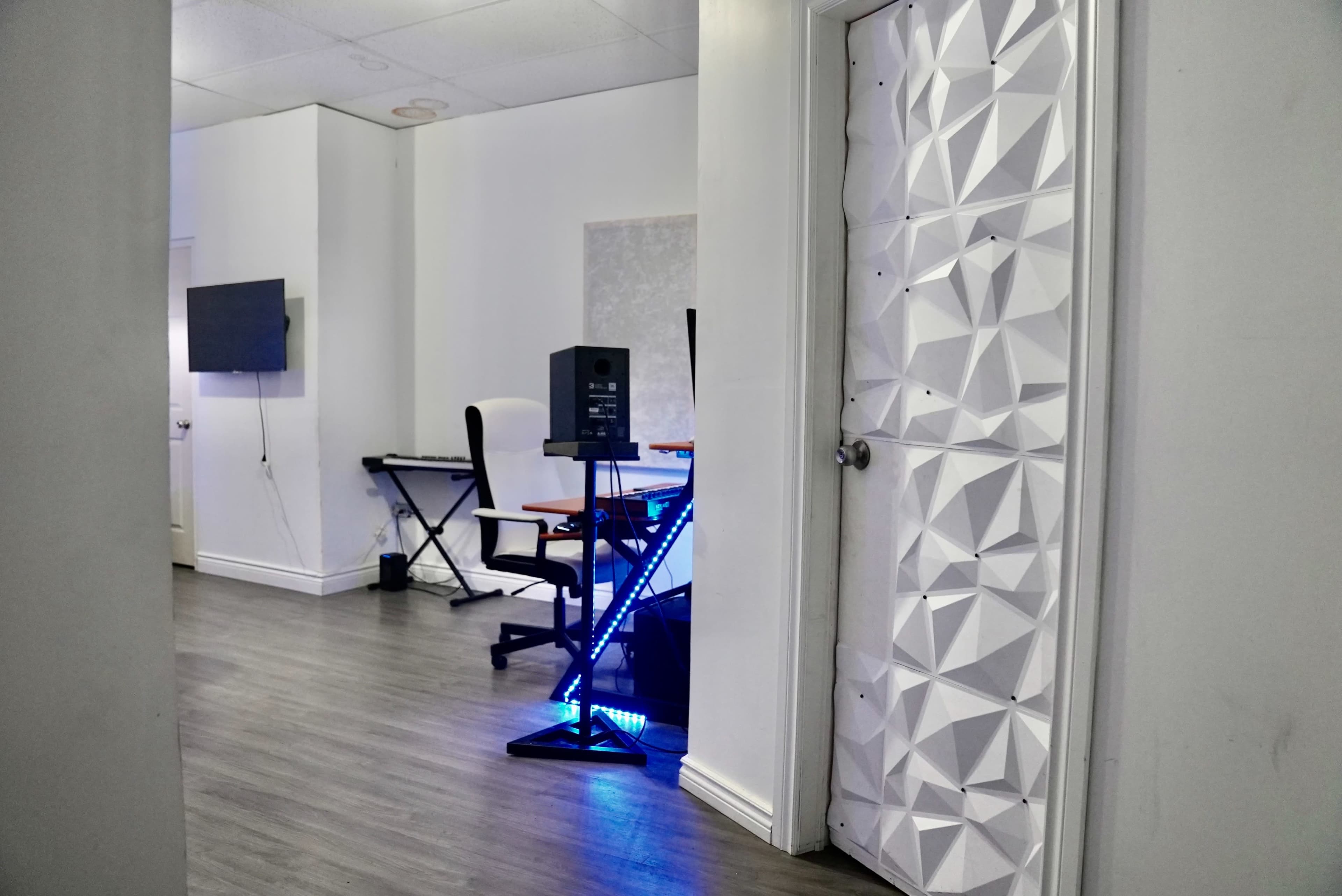 A modern interior space with a white door featuring a textured design, a desk with a computer setup, and a wall-mounted screen.