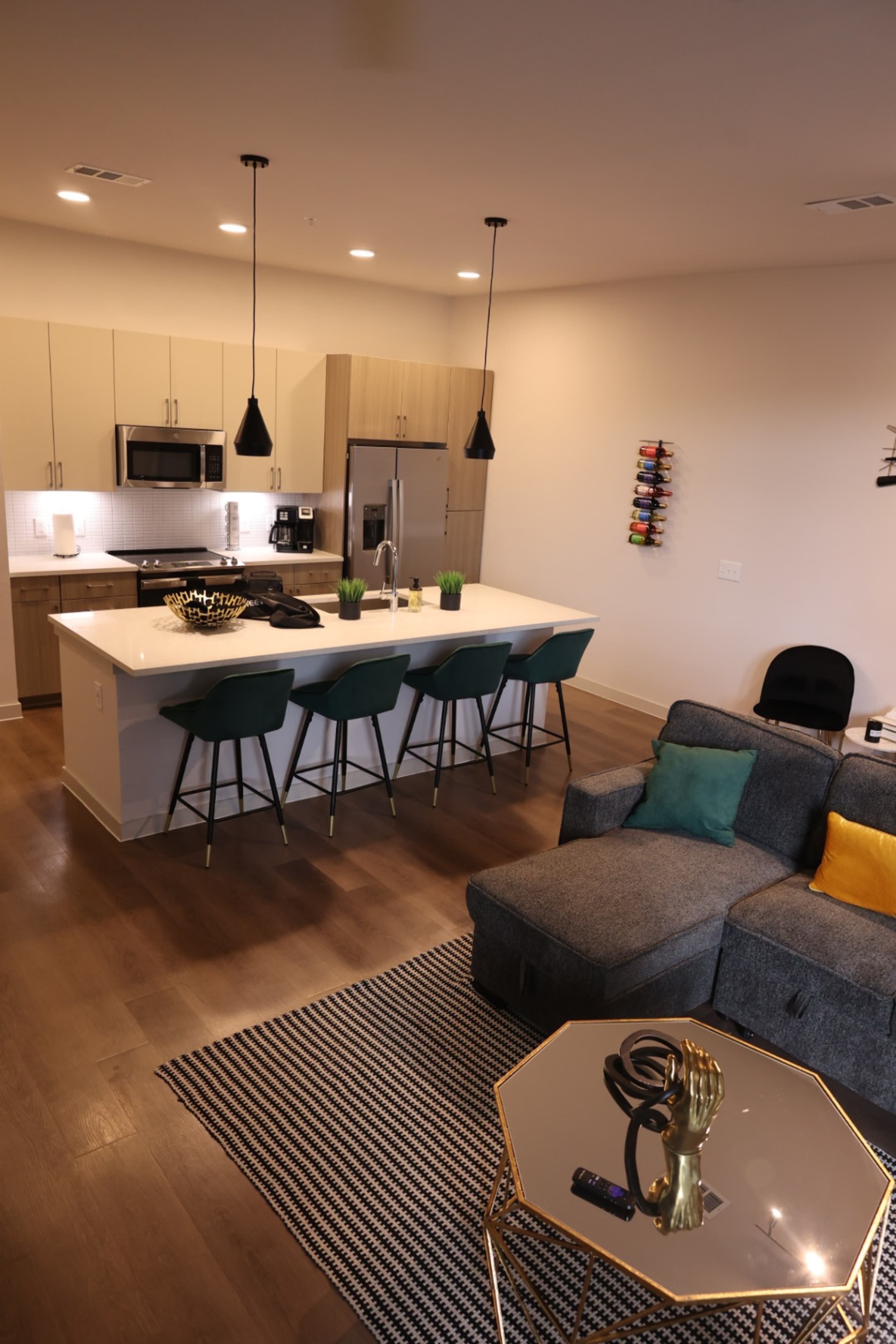 A modern open-concept kitchen and living area with a bar seating island, a gray sectional sofa, and decorative elements like a geometric coffee table and patterned rug.