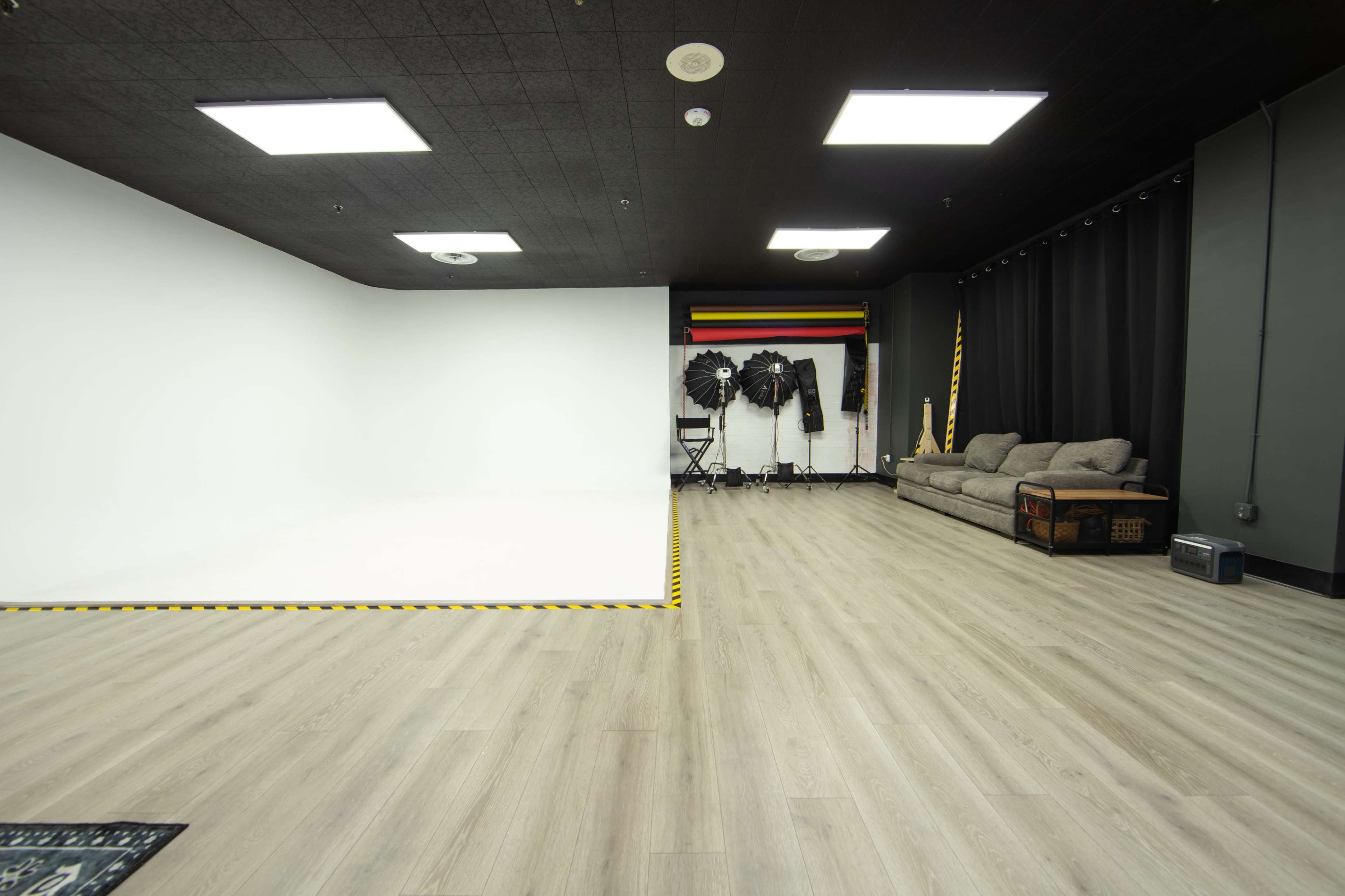 The image shows a photography studio with a white backdrop on one side, a gray couch, and various equipment arranged on the other side.