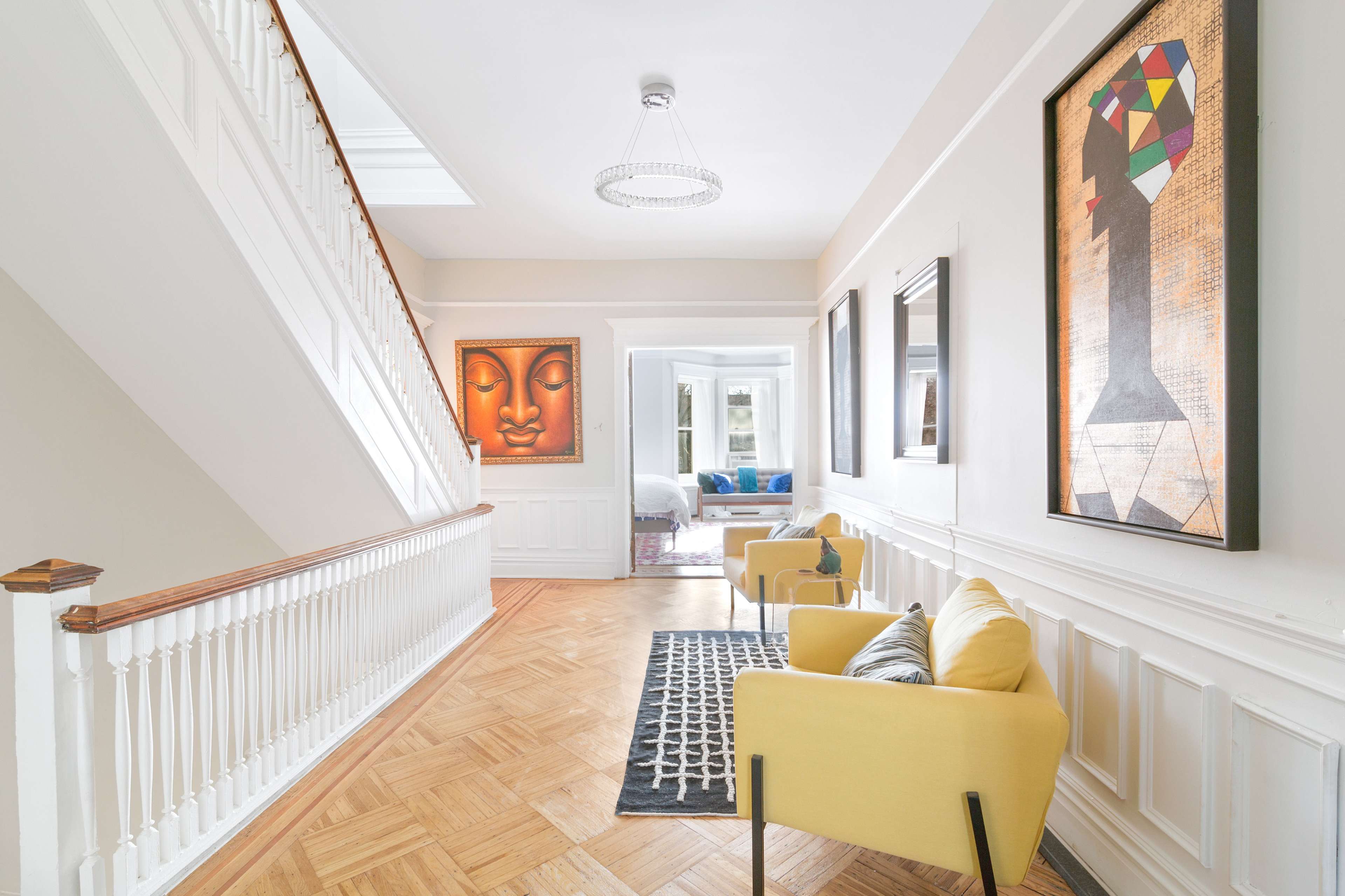 A spacious hallway with a staircase, featuring yellow armchairs and framed artwork on the walls.