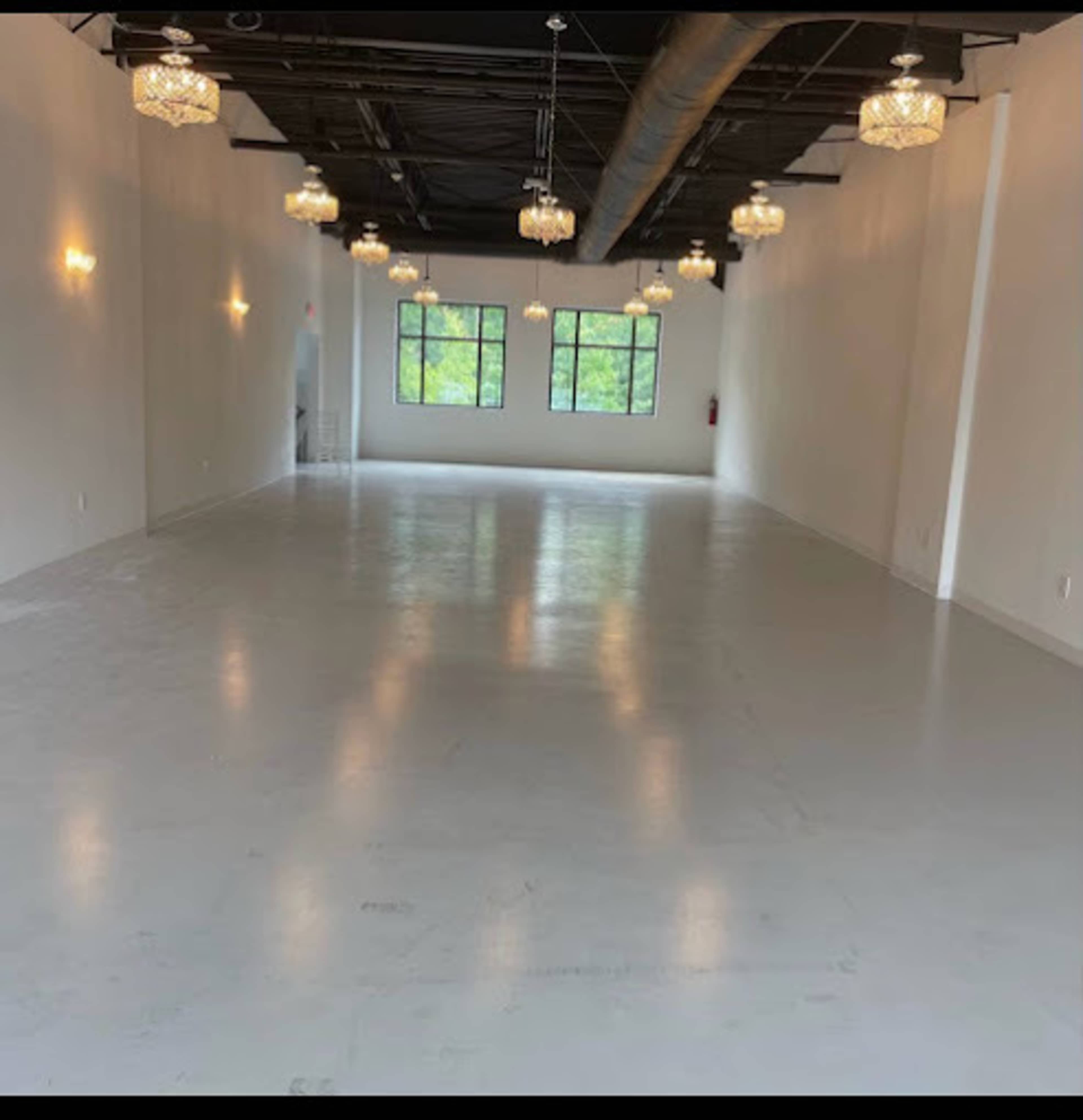The image shows a spacious, empty room with white walls and a polished floor, illuminated by multiple hanging chandeliers and wall sconces.