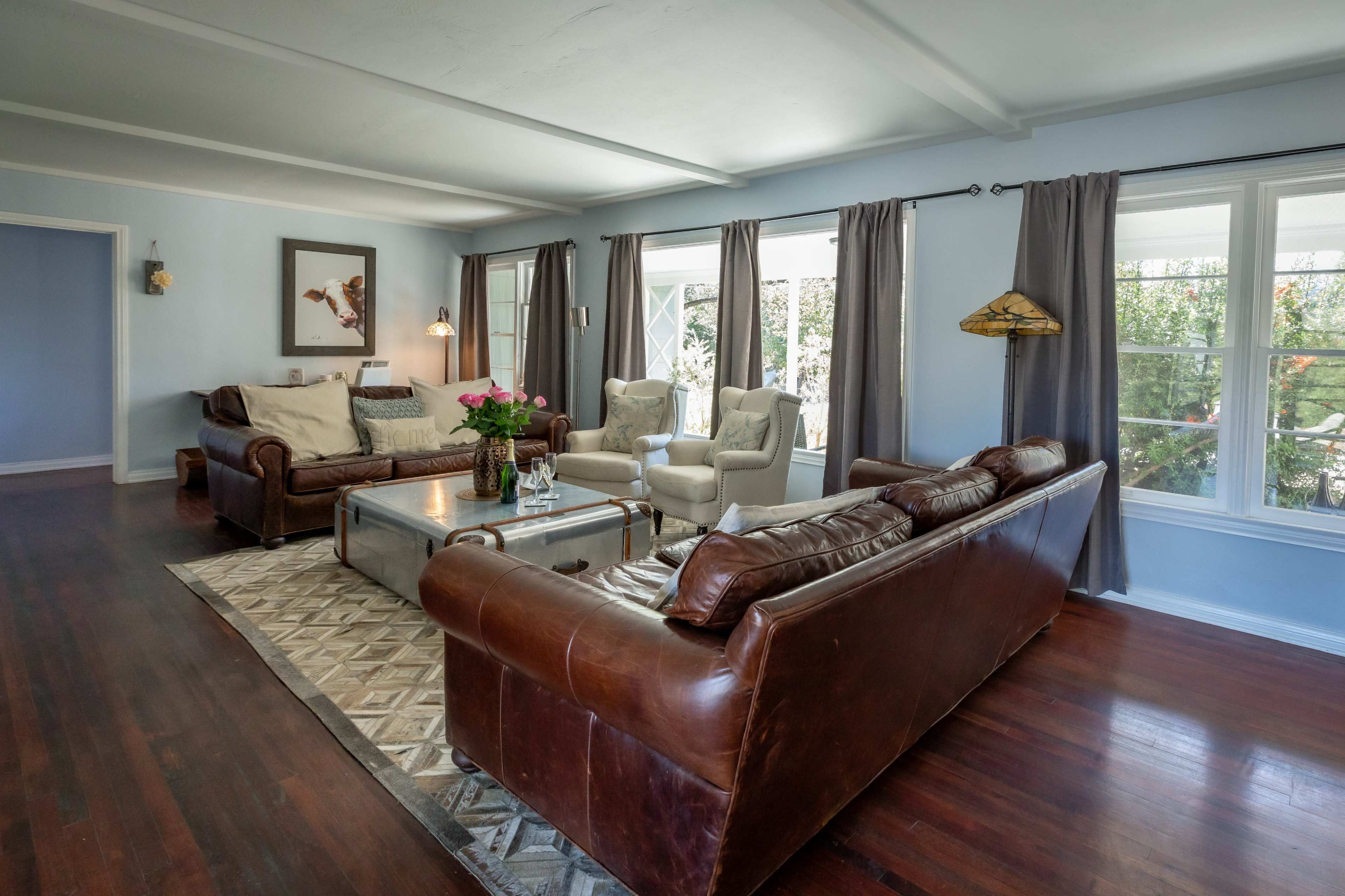 A living room with two leather sofas, a glass coffee table, and large windows covered with curtains.
